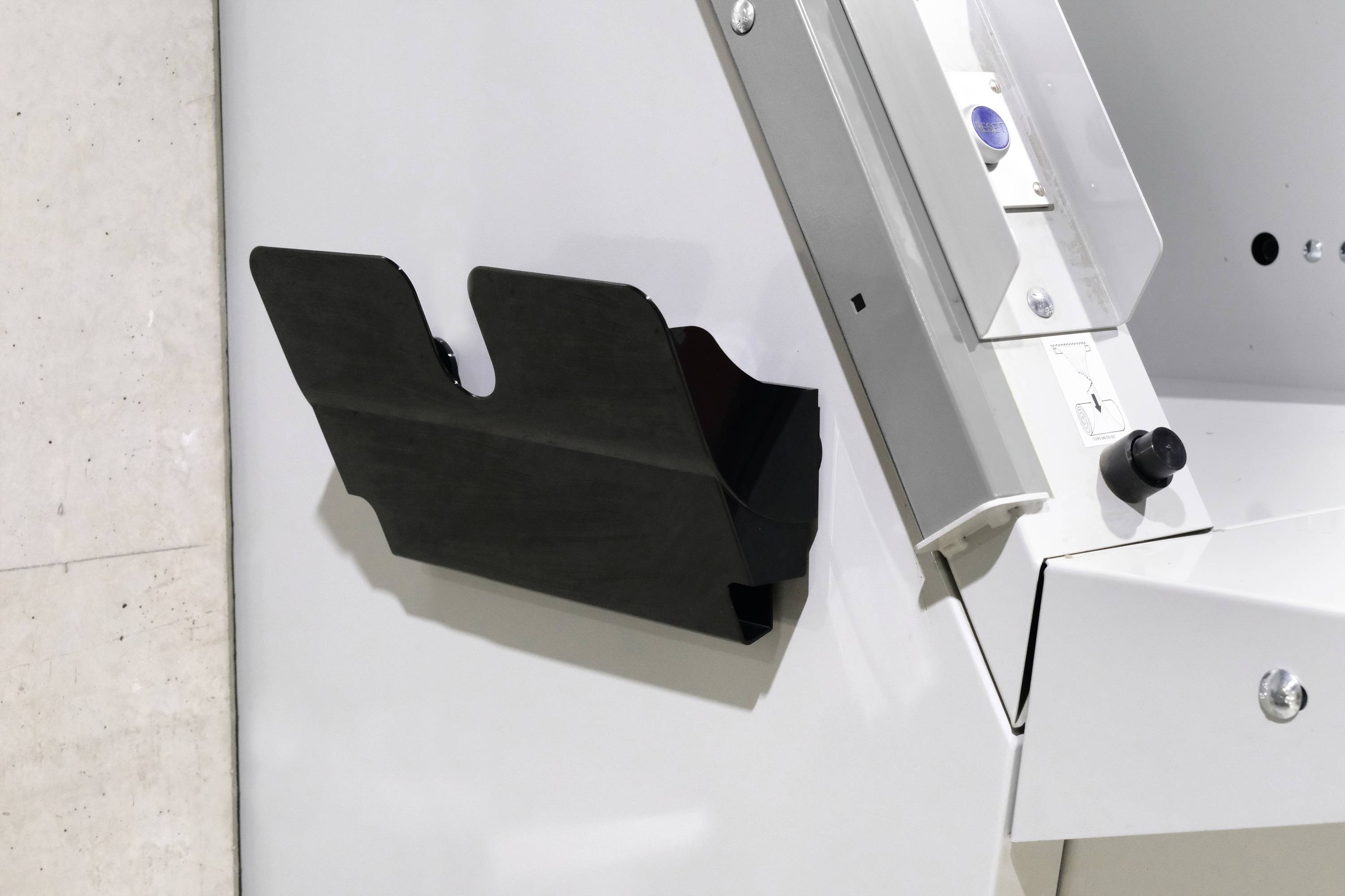Schwarze Ablagehalterung an einem weißen Fotokopierer befestigt, neben Tastenfeld und Papierausgabeplatz.