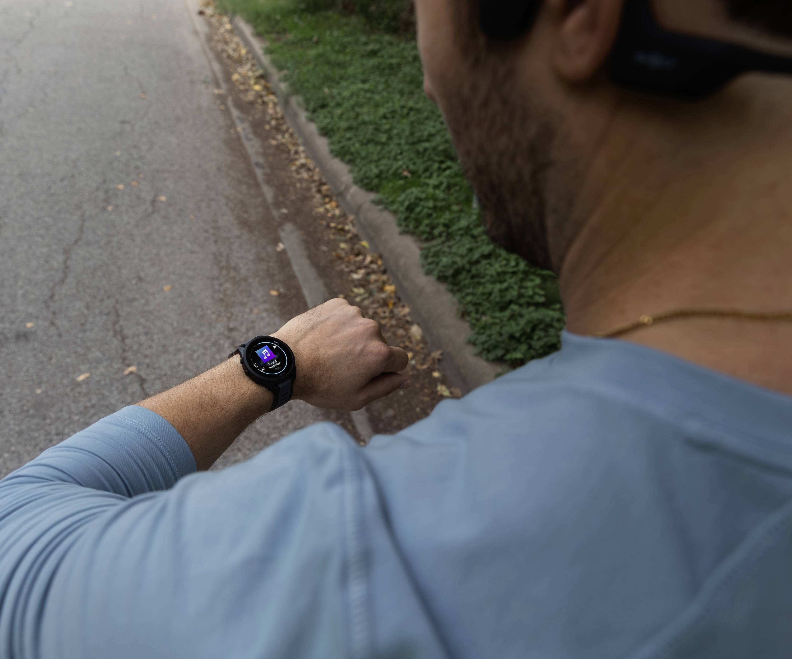Ein Mann in Sportkleidung schaut beim Laufen auf seine Smartwatch, die Trainingsdaten anzeigt. Er befindet sich auf einer Straße.
