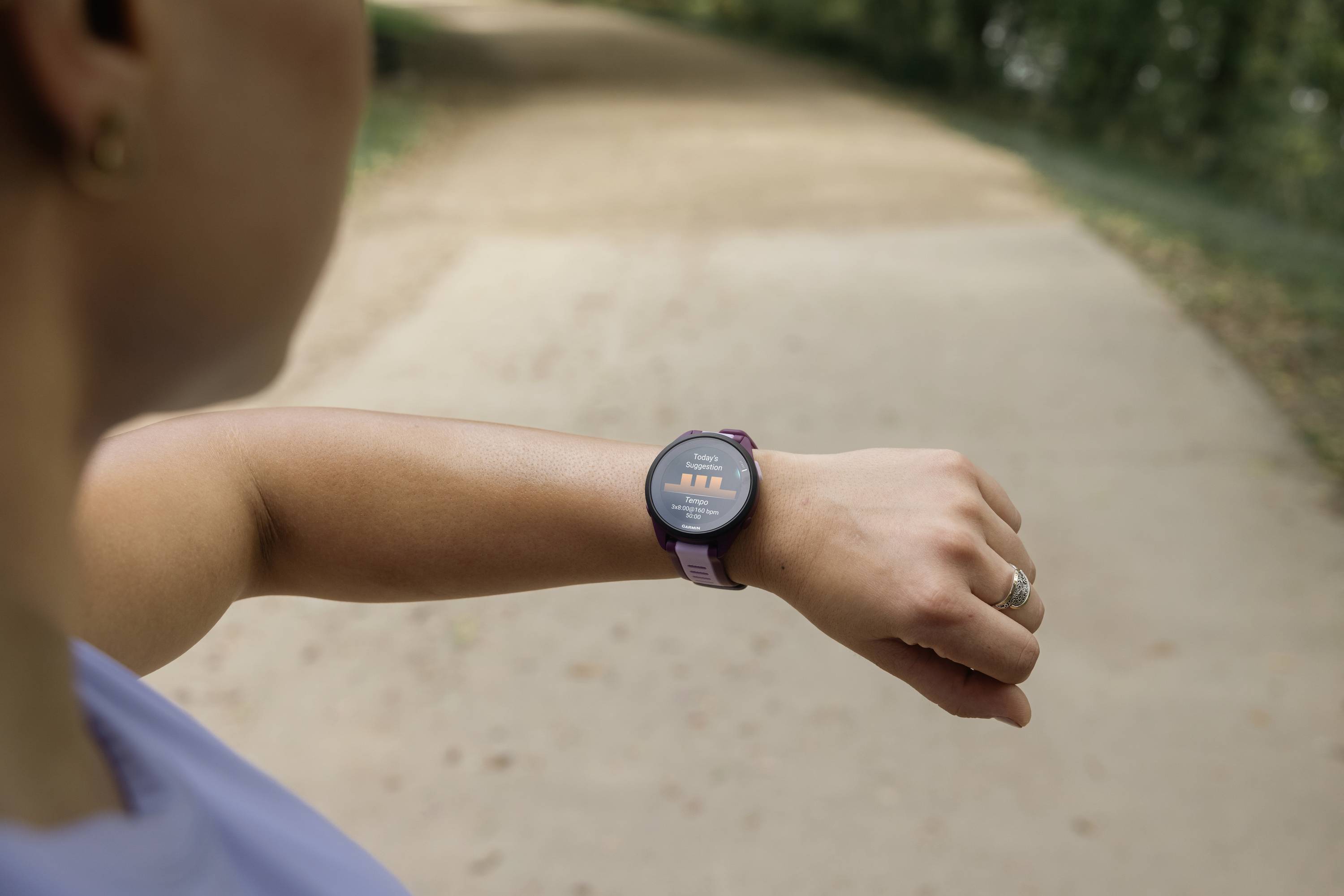 Eine Person schaut auf eine Smartwatch beim Laufen auf einem Weg im Freien. Die Uhr zeigt Fitnessdaten an.