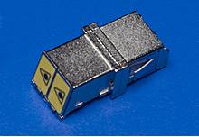Metallischer Steckverbinder auf blauem Hintergrund, mit zwei gelben Dreiecken an der Spitze.