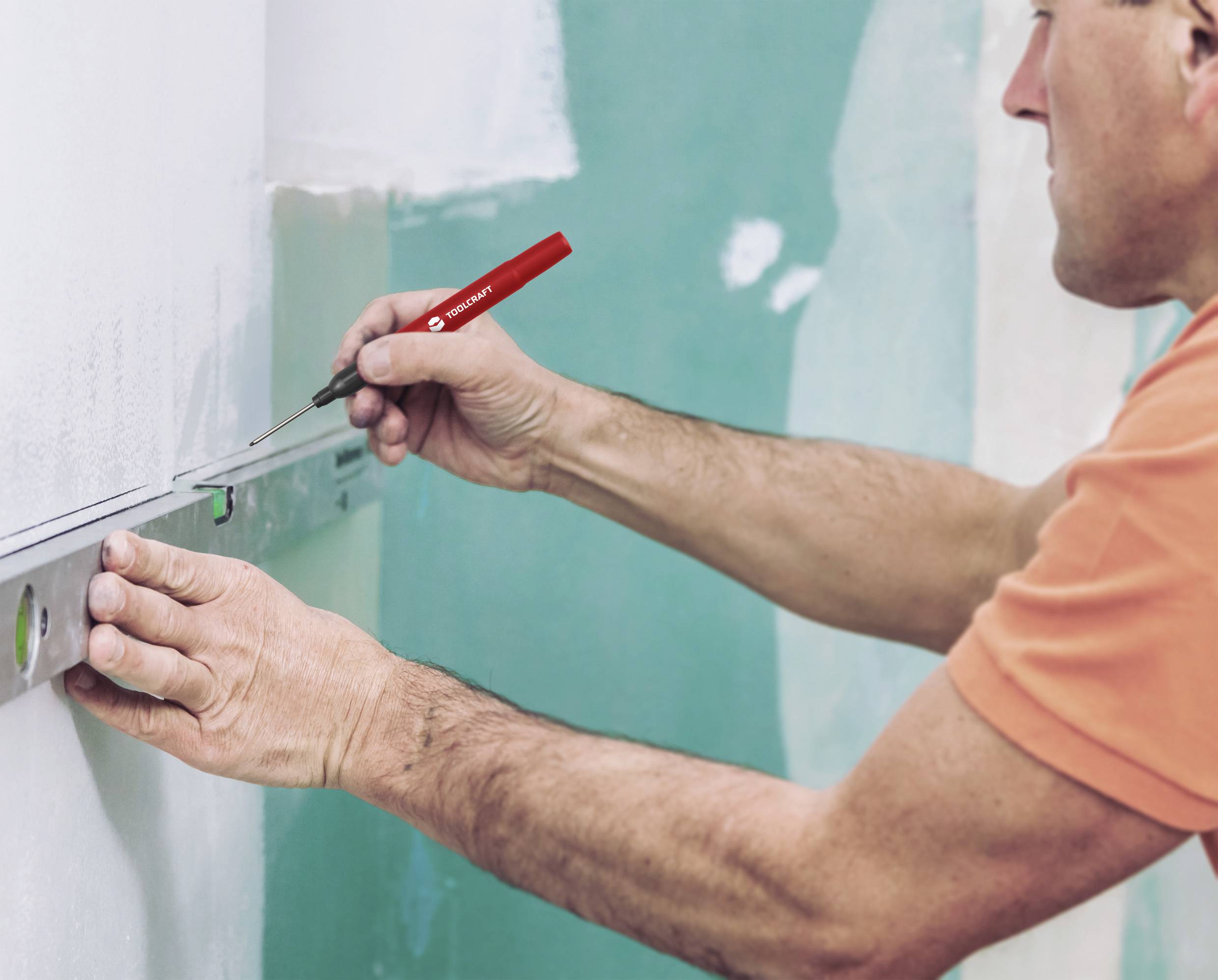 Ein Mann misst mit einer Wasserwaage und markiert eine Linie an der Wand.