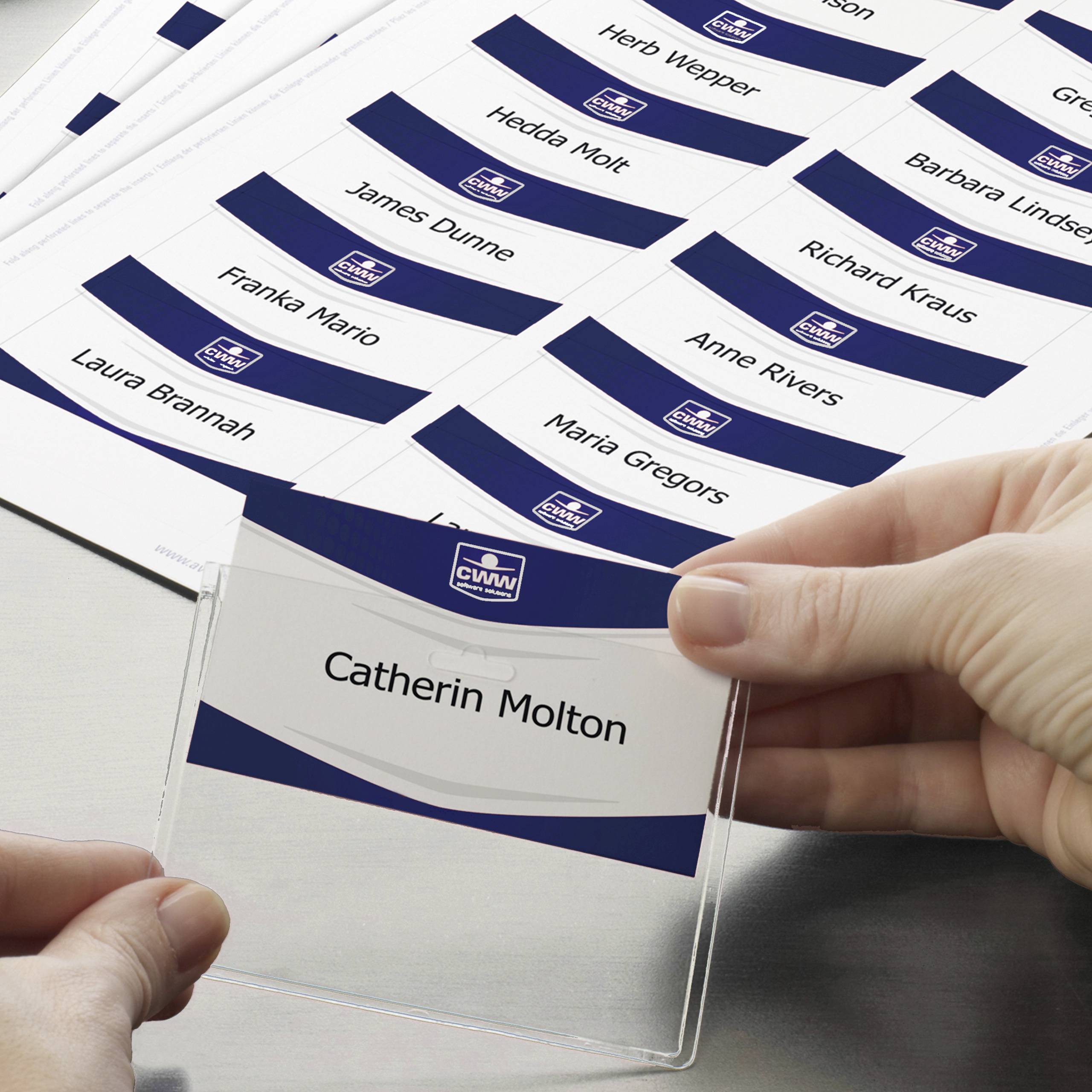 Eine Hand legt ein Namensschild mit der Aufschrift 'Catherine Molton' in einen Halter ein. Im Hintergrund sind weitere Namensschilder.