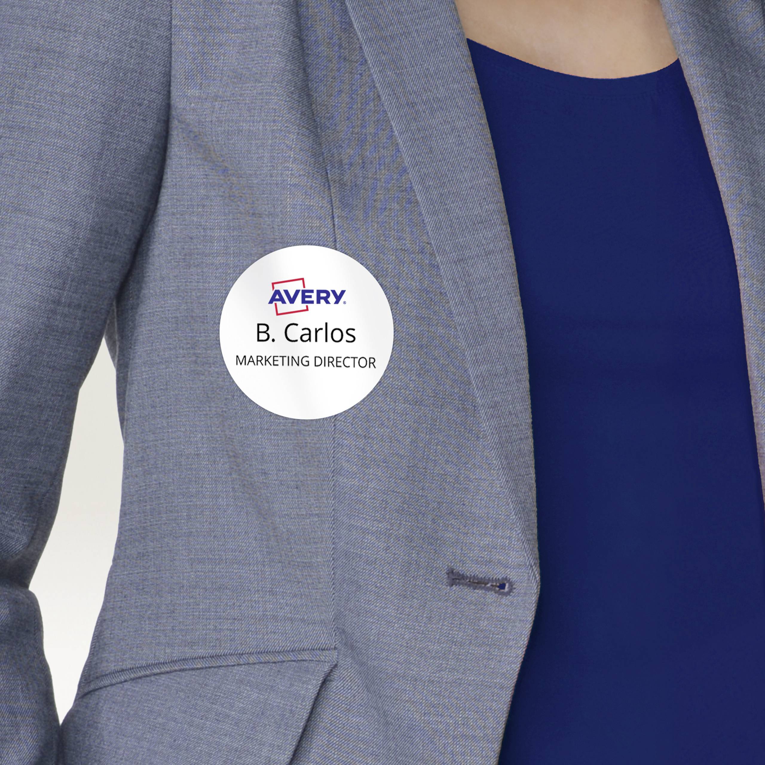 Eine Person trägt ein Namensschild mit der Aufschrift 'B. Carlos, Marketing Director' auf einem grauen Blazer über einem blauen Hemd.