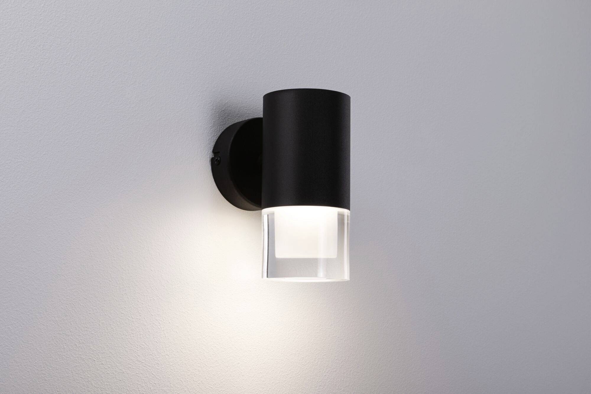 Schwarze Wandlampe leuchtet an einer hellen Wand, modern und minimalistisch gestaltet, strahlt warmes Licht nach unten aus.