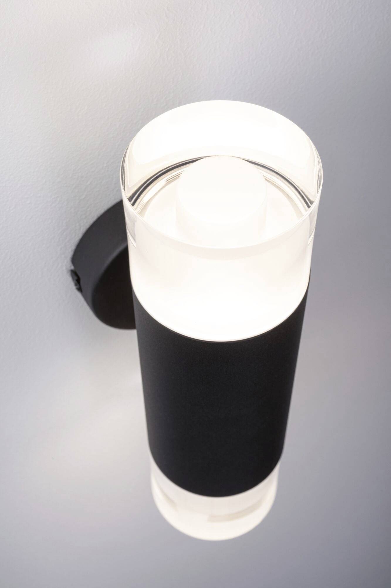 Eine moderne Wandleuchte mit zylindrischer Form, schwarzem Gehäuse und leuchtendem, hellem Licht, montiert an einer Wand.