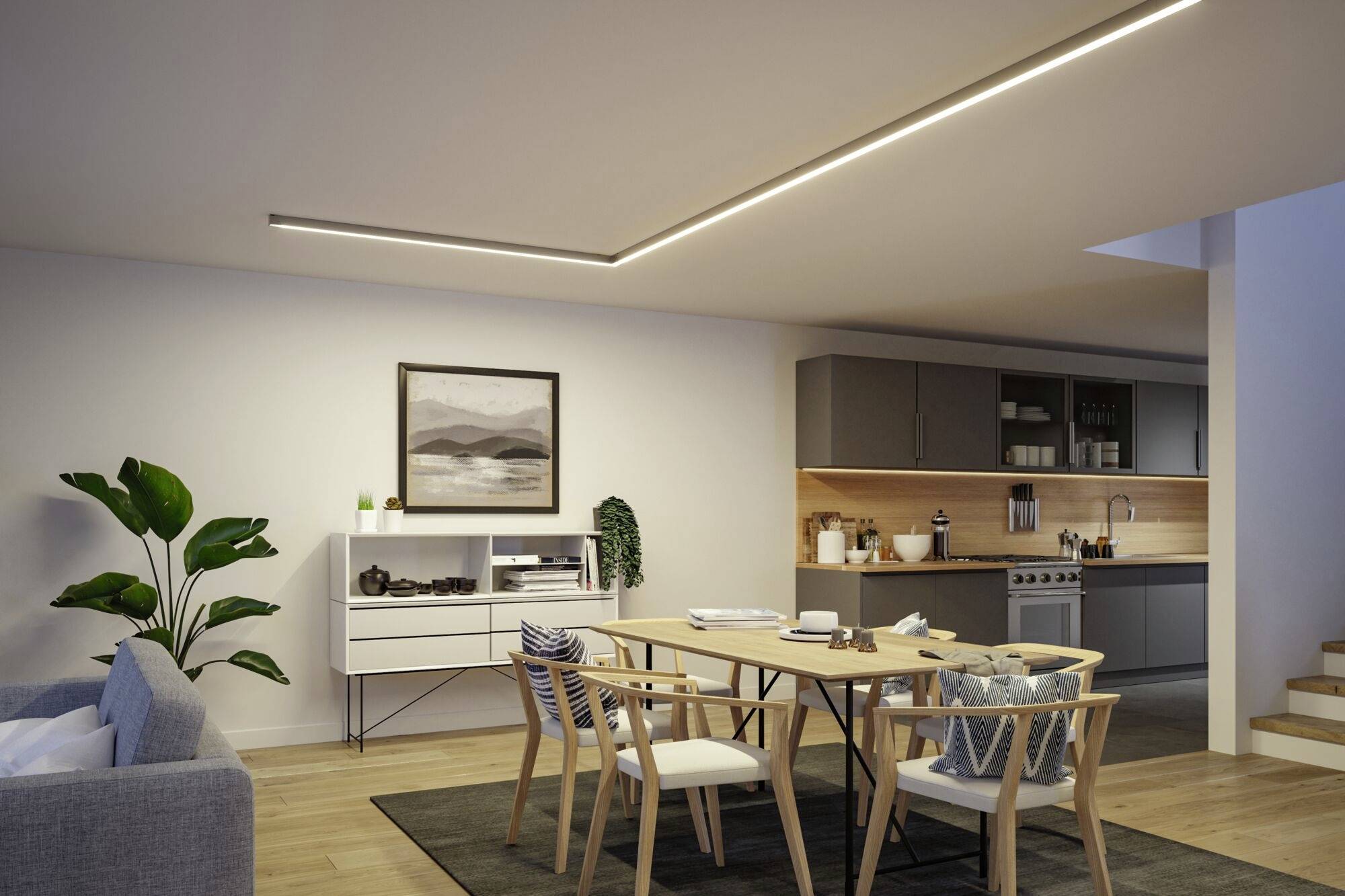 Modernes Wohnzimmer mit Esstisch, Stühlen und grauem Sofa. Offene Küche im Hintergrund. Dezente Beleuchtung und Wandkunst.