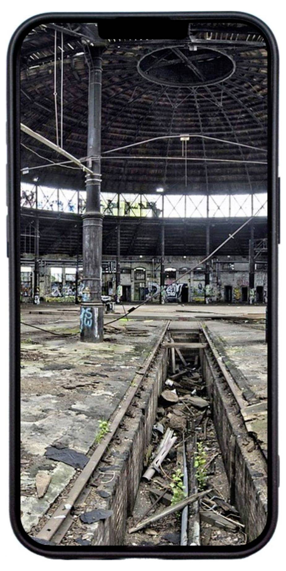 Ein altes, verlassenes Fabrikgebäude mit stark beschädigten Böden und Graffiti an den Wänden. Pflanzen wachsen zwischen den zerbrochenen Bodenplatten.