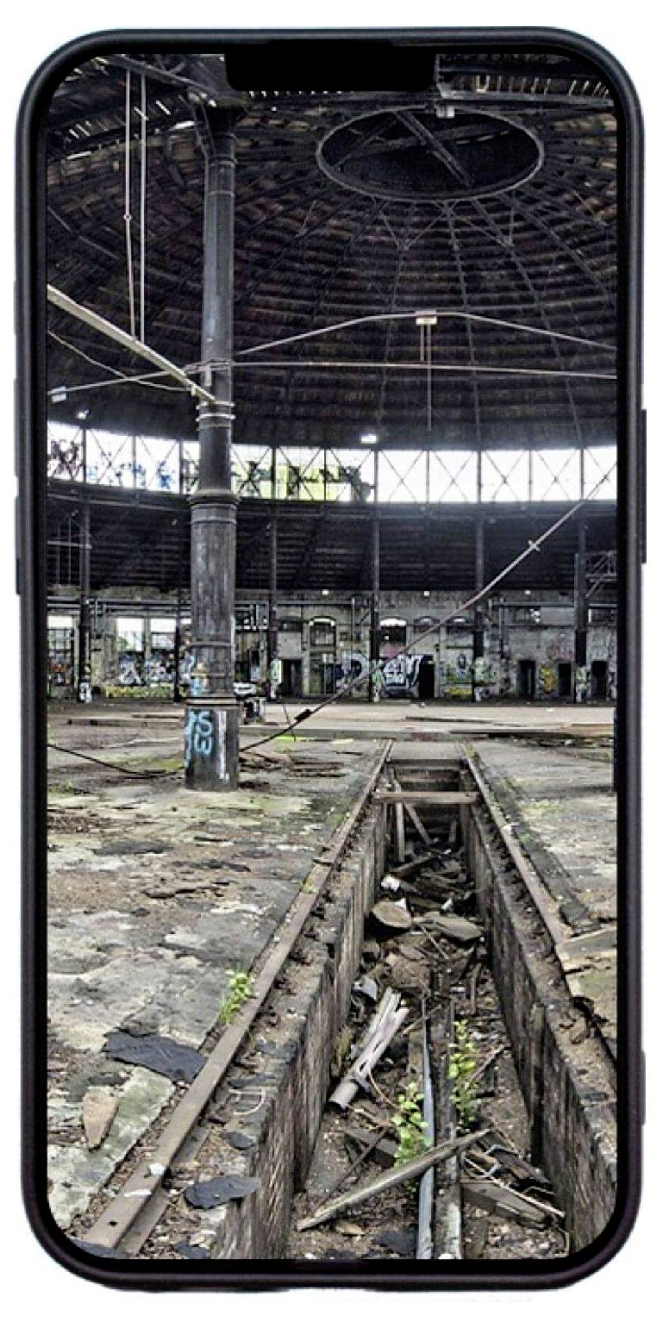 Ein altes, verfallenes Industriegebäude mit Graffiti an den Wänden, betrachtet durch den Bildschirm eines Smartphones.