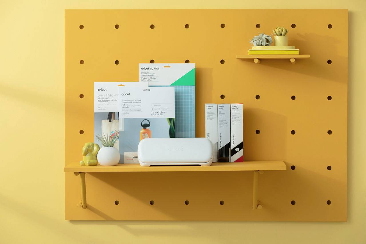 Kreativ-Ecke mit gelbem Regal, das eine Pflanze, Kunstzubehör-Verpackungen und ein weißes Gerät präsentiert.