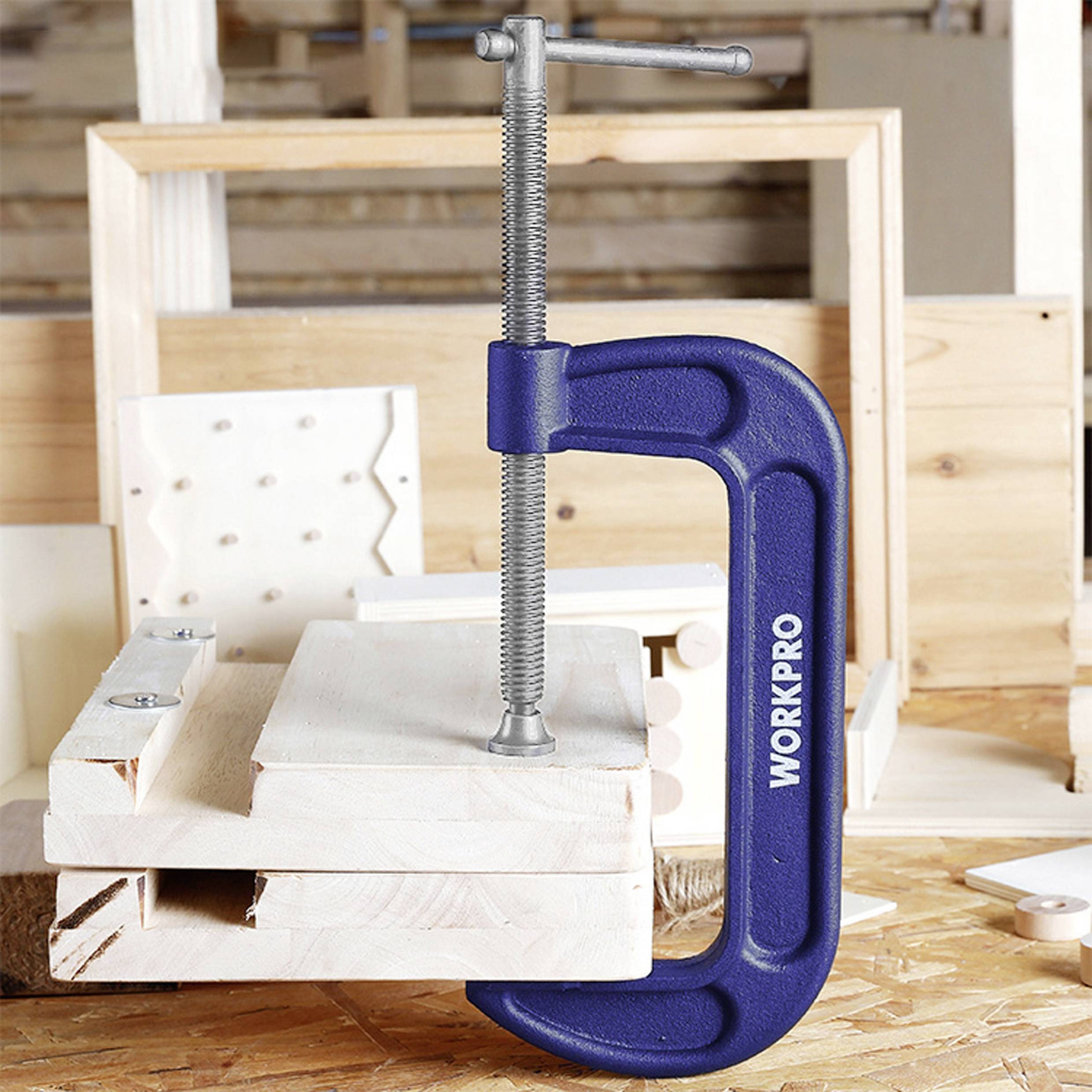 Eine blaue Schraubzwinge hält mehrere Holzbretter zusammen, die auf einer Werkbank in einer Holzwerkstatt liegen.
