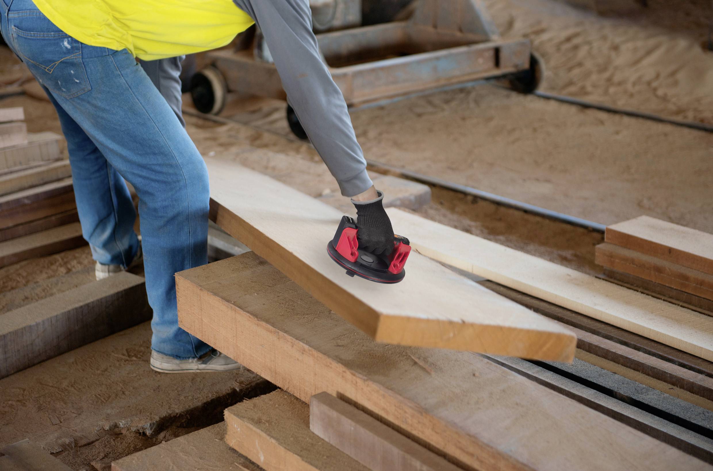 Person schleift Holzbretter mit einem Handschleifer in einer Werkstatt. Es handelt sich um eine handwerkliche Tätigkeit.