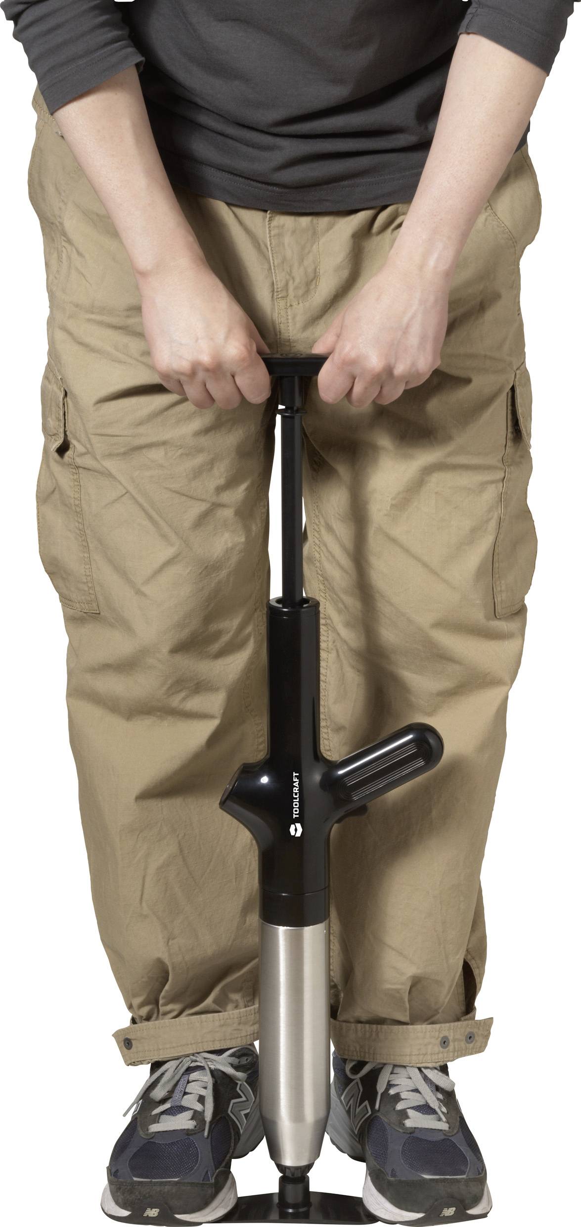 Eine Person pumpt Luft mit einer Handpumpe. Sie trägt beigefarbene Hosen und Turnschuhe.