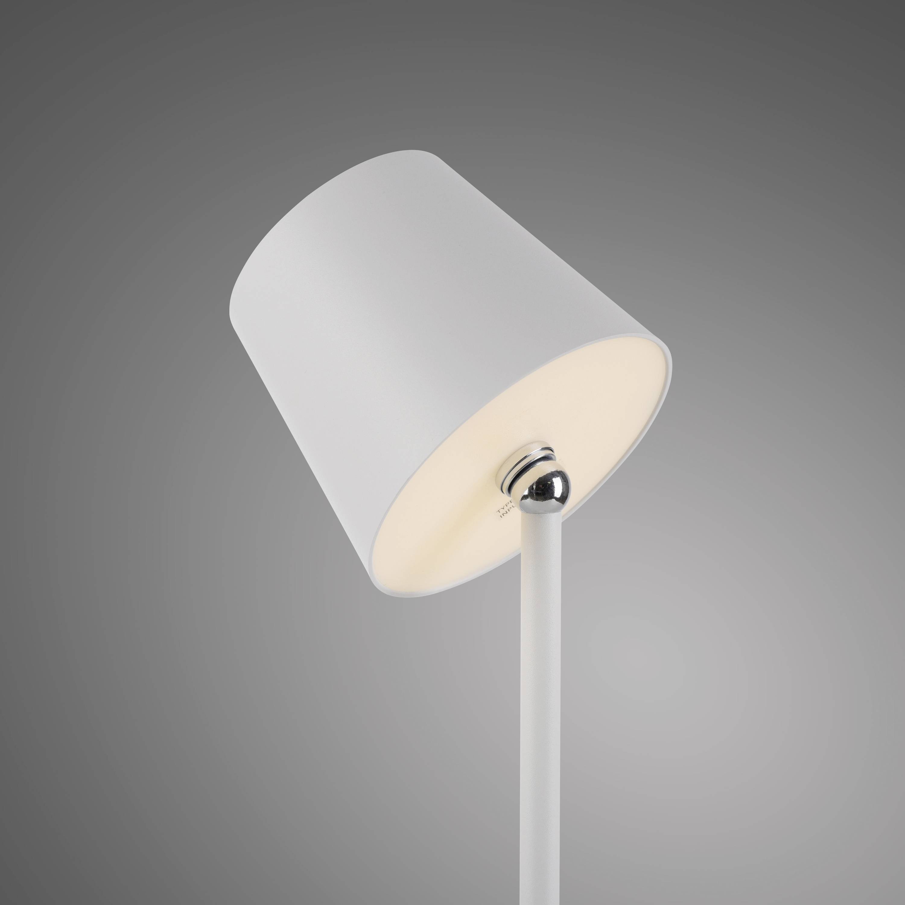 Eine moderne, weiße Stehlampe mit zylindrischem Schirm und Metallstange, leuchtet warmes Licht aus. Vor grauem Hintergrund.