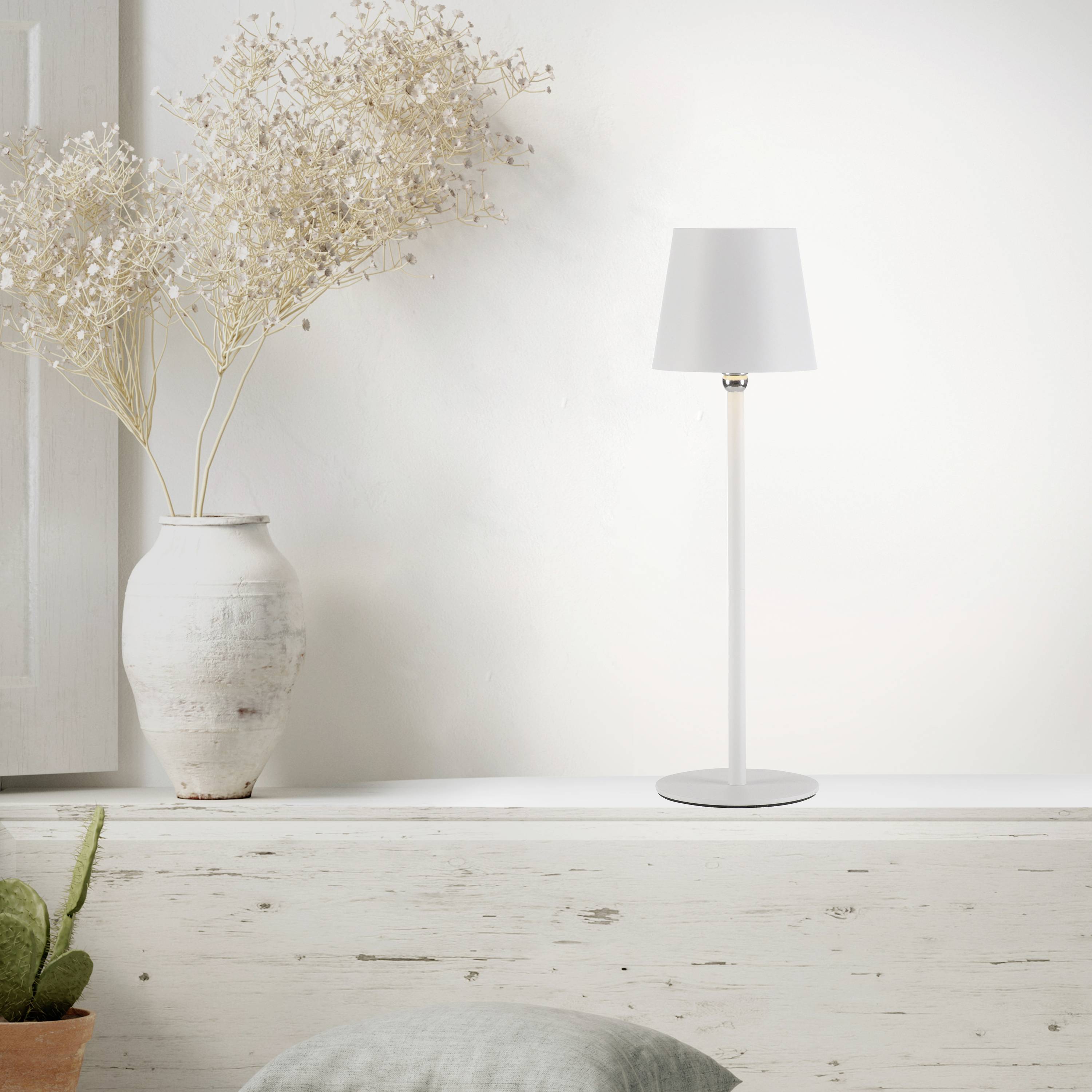 Ein weißer Tisch mit einer Vase voller getrockneter Blumen und einer modernen weißen Lampe; minimalistische Inneneinrichtung.