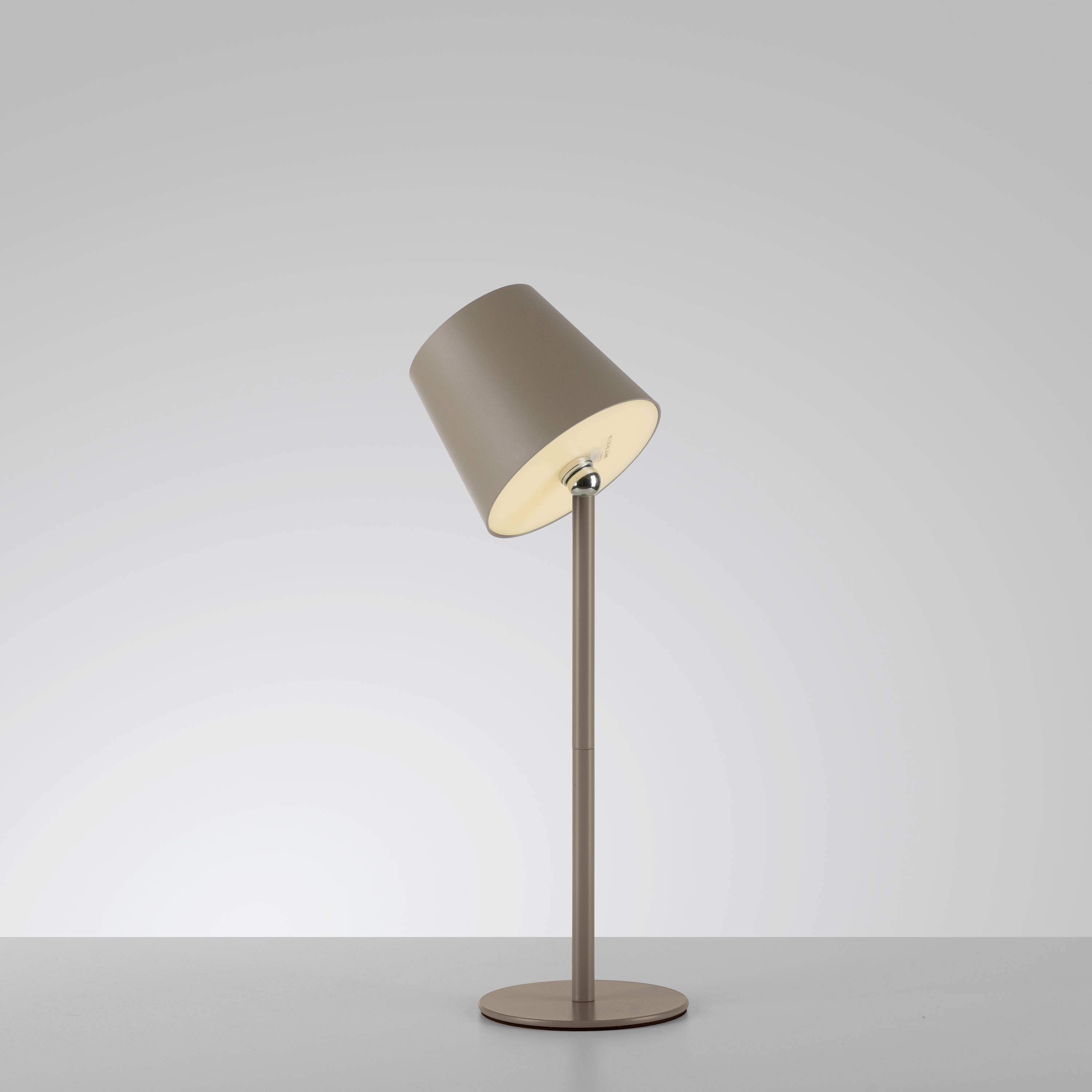 Stehlampe mit schlichtem Design, braunem Schirm, auf rundem Sockel, beleuchtet weißen Hintergrund.