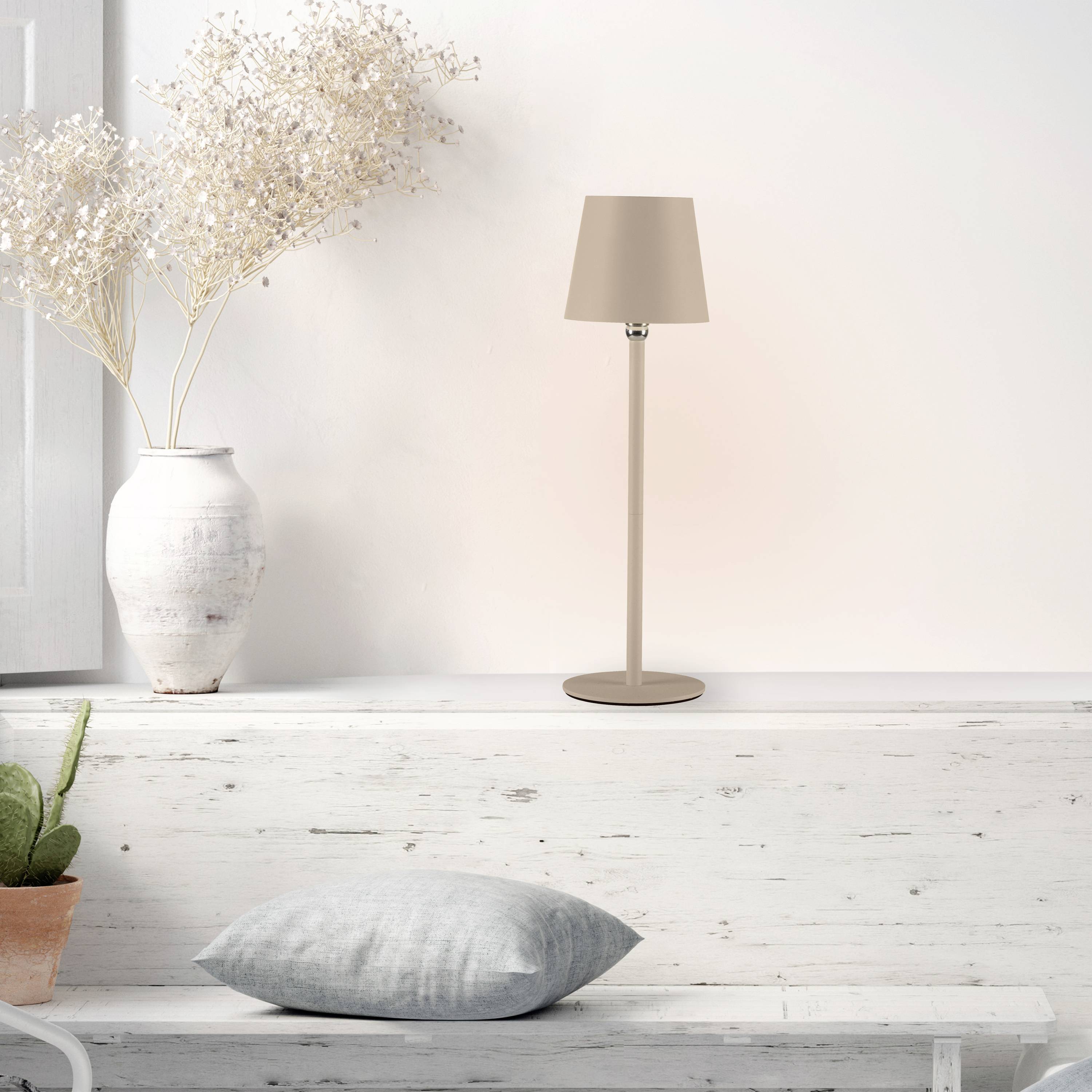 Ein minimalistischer Raum mit einer braunen Tischlampe und einer weißen Vase mit Trockenblumen auf einem hellen Holzregal.