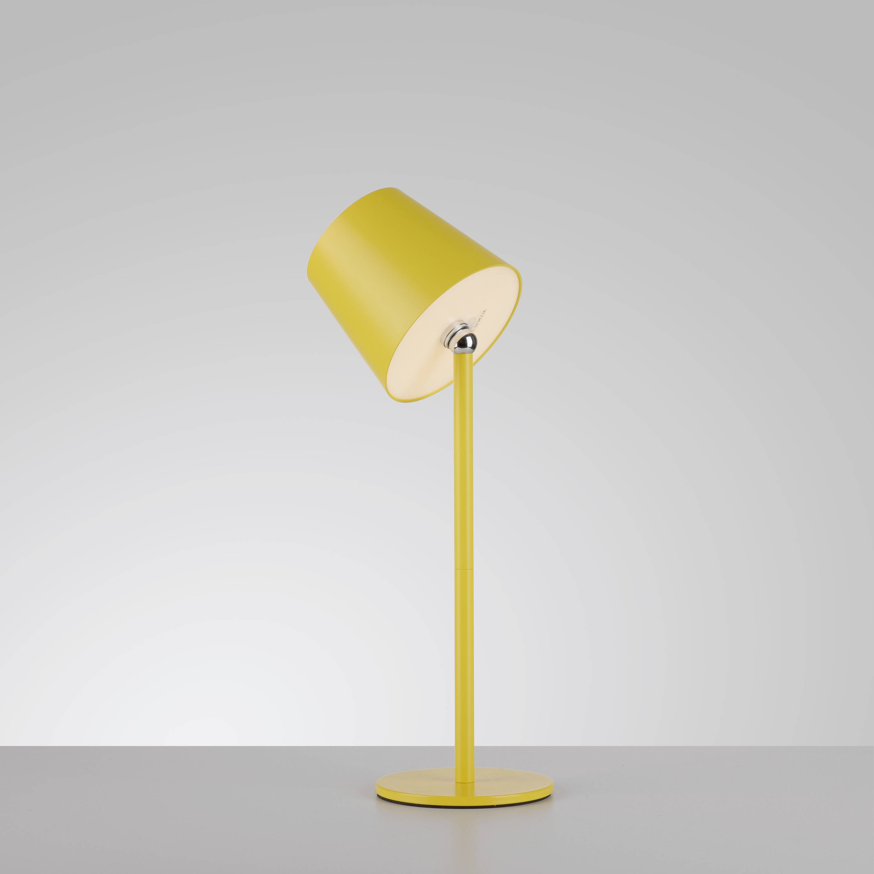 Gelbe Tischlampe mit zylindrischem Schirm, geneigt auf einem dünnen Stab, vor grauem Hintergrund.