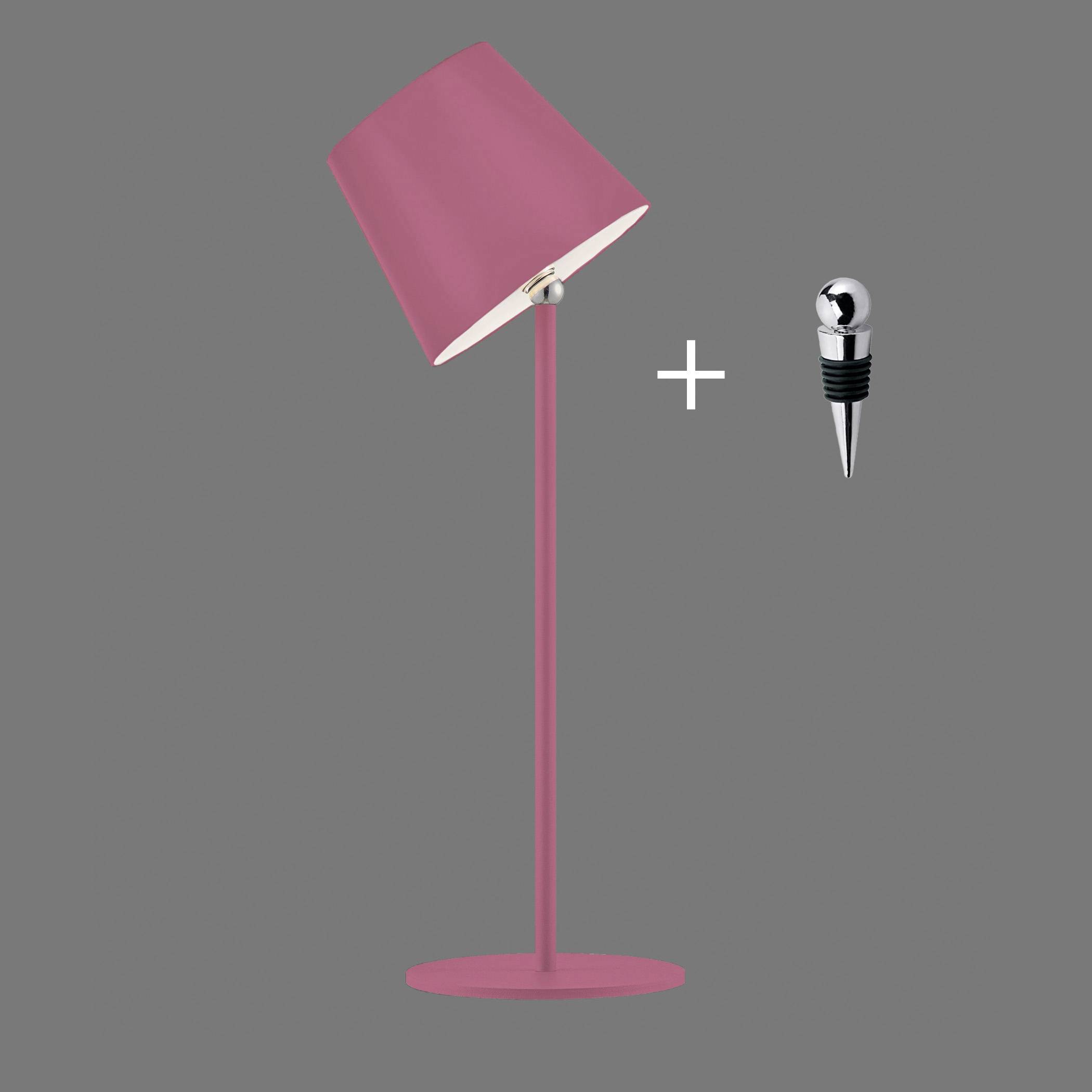 Rosa Tischlampe mit schrägem Schirm steht auf grauem Hintergrund, daneben ein silberner Weinverschluss mit Kreuzmotiv.
