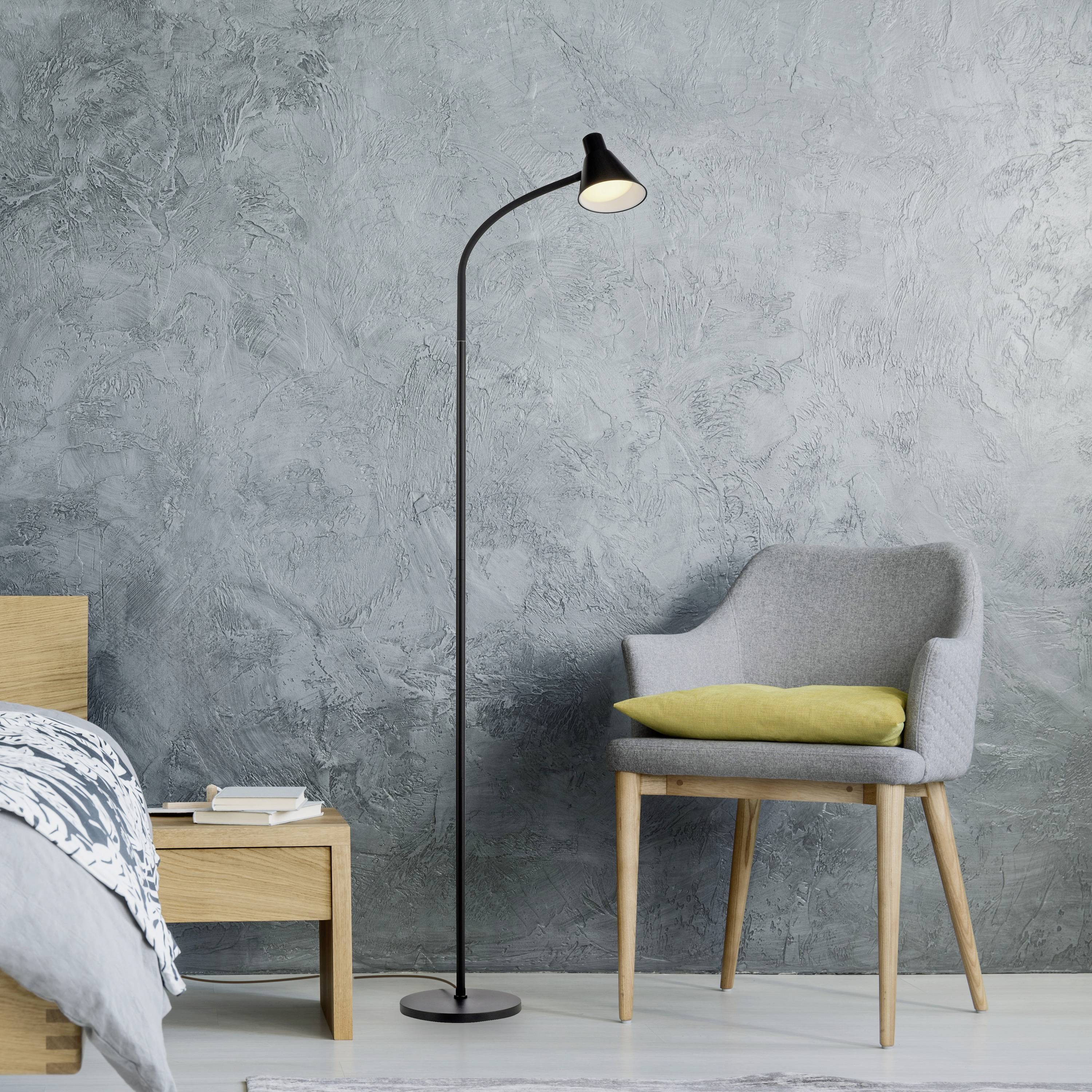 Stehlampe neben grauem Sessel und Holztisch mit Büchern, vor einer grauen Wand.