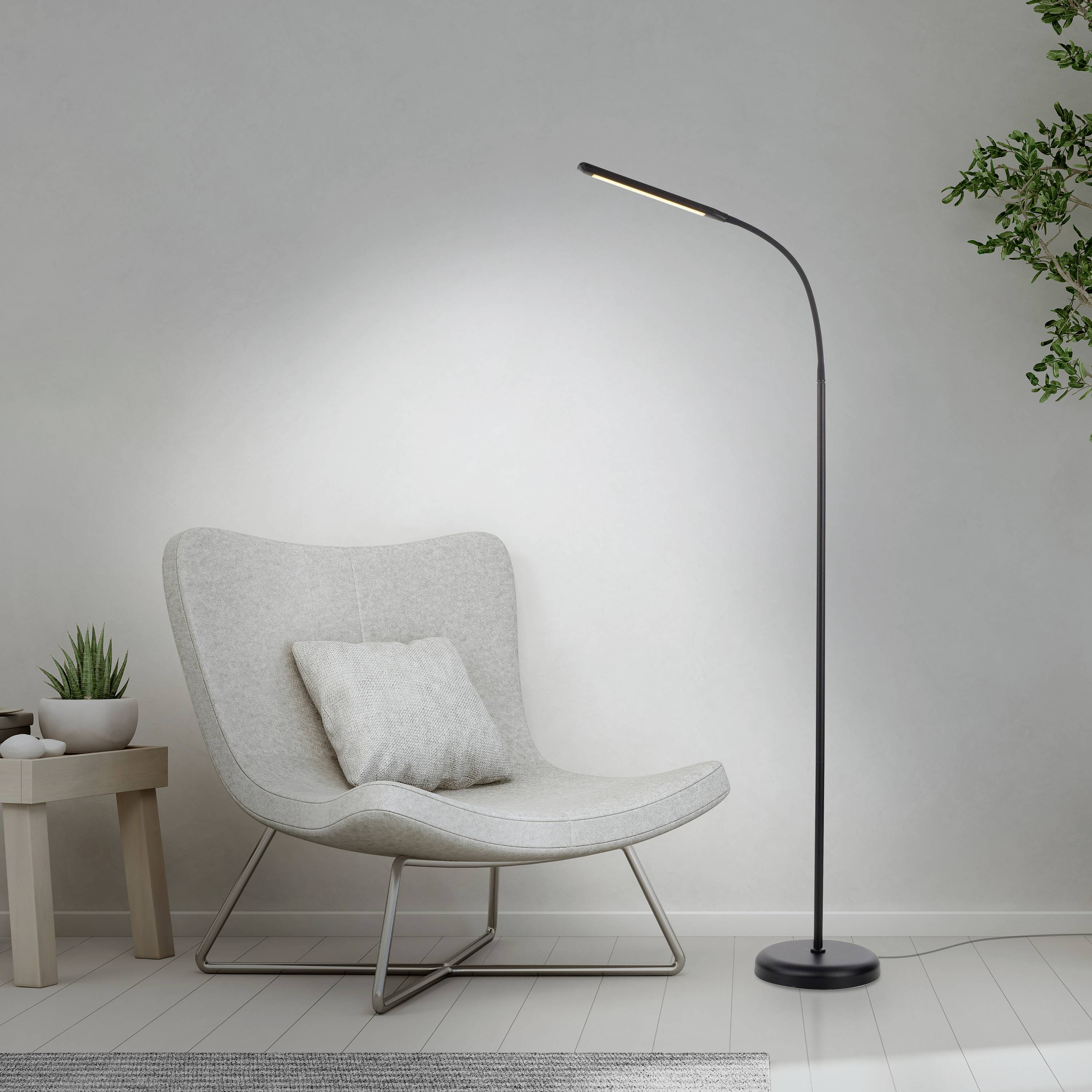 Ein moderner, heller Raum mit einem grauen Sessel und einer schlanken Stehlampe. Daneben ein Holztisch mit einer Pflanze.