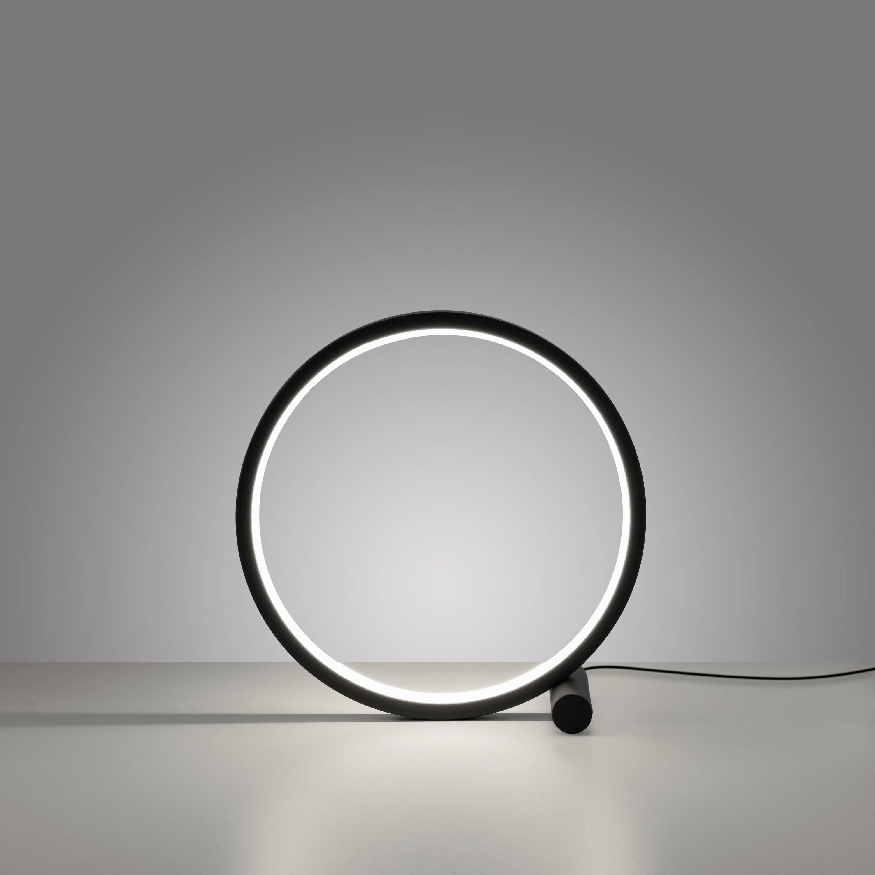 Ein minimalistisch gestalteter, kreisförmiger Tischleuchte mit LED-Licht auf einer glatten Oberfläche, ohne sichtbare Details im Hintergrund.