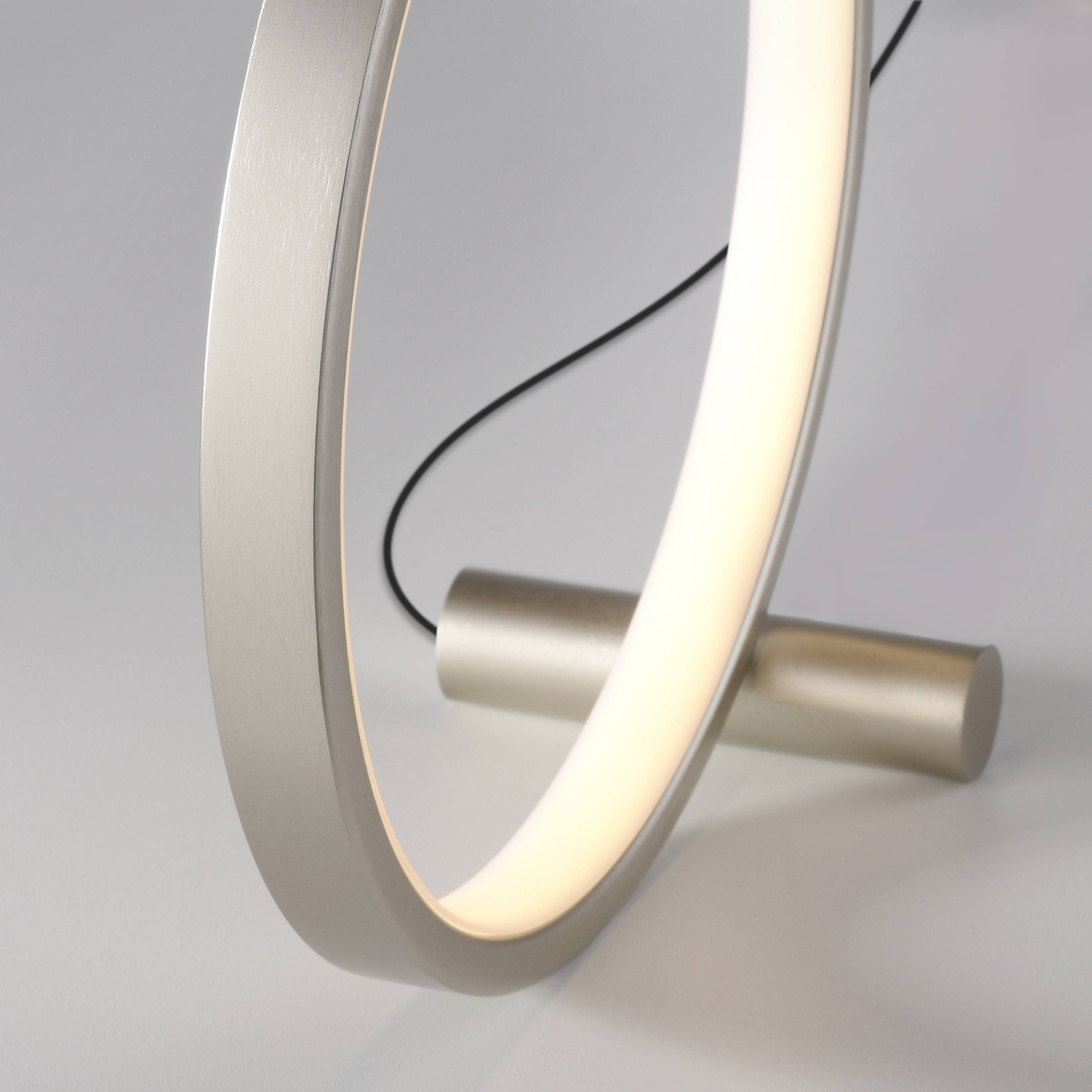 Beleuchtete, moderne Tischlampe mit rundem Ringdesign und gebürsteter Metalloberfläche auf weißem Hintergrund.