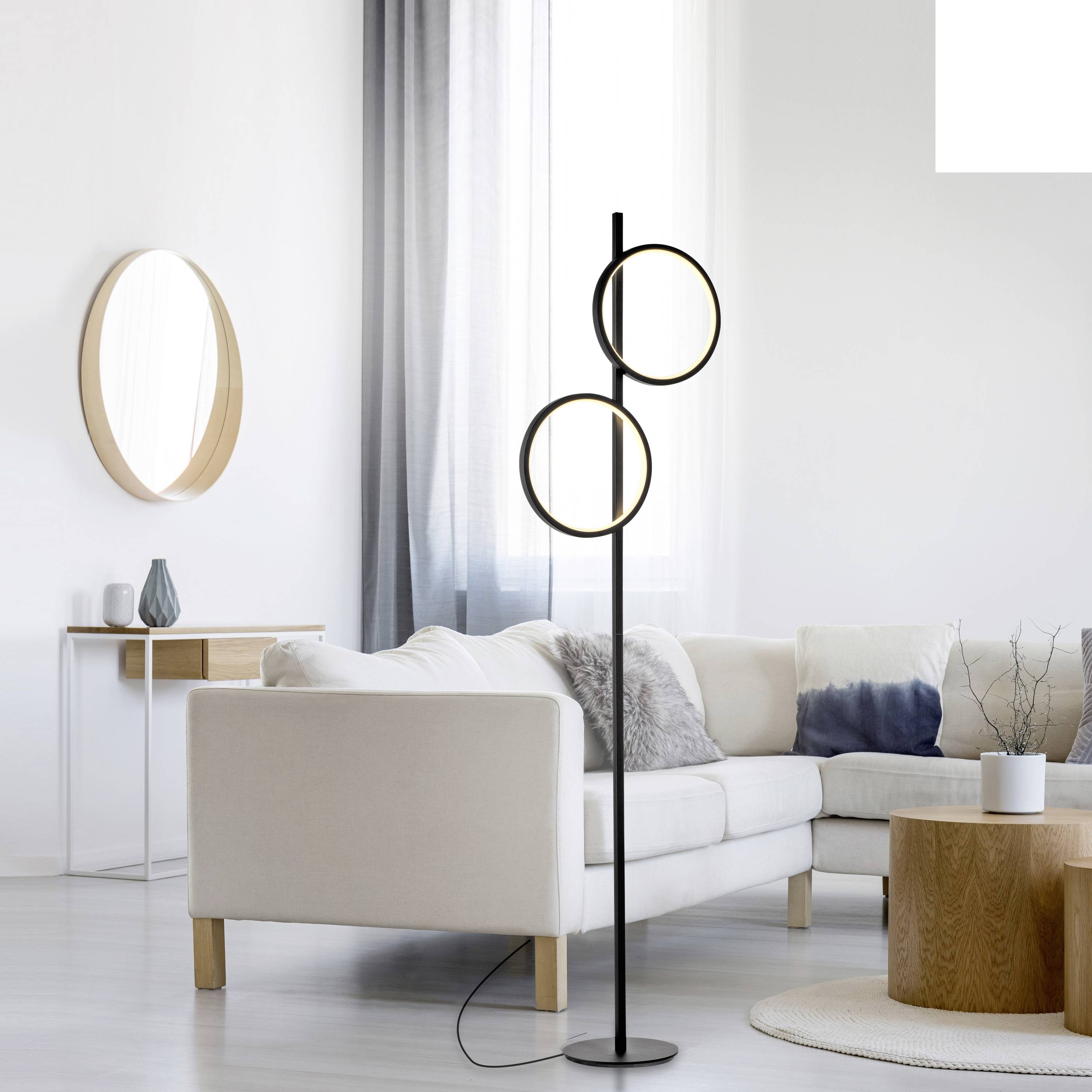 Ein modernes Wohnzimmer mit hellen Farbtönen, einem cremefarbenen Sofa, einem runden Spiegel an der Wand und einer Stehleuchte.