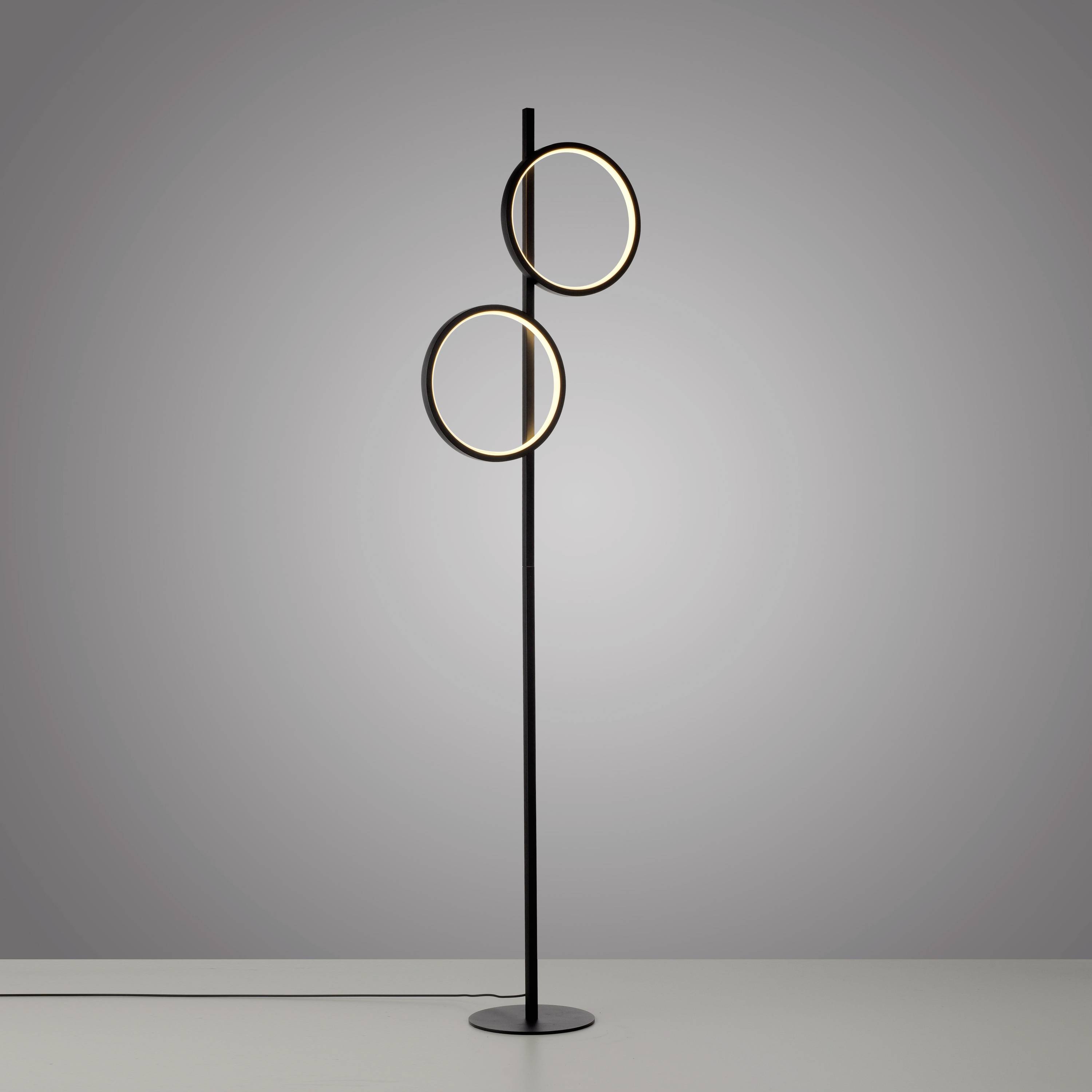Schlanke, moderne Stehlampe mit zwei schwebenden, kreisförmigen Leuchtringen in einem schlichten Raum.