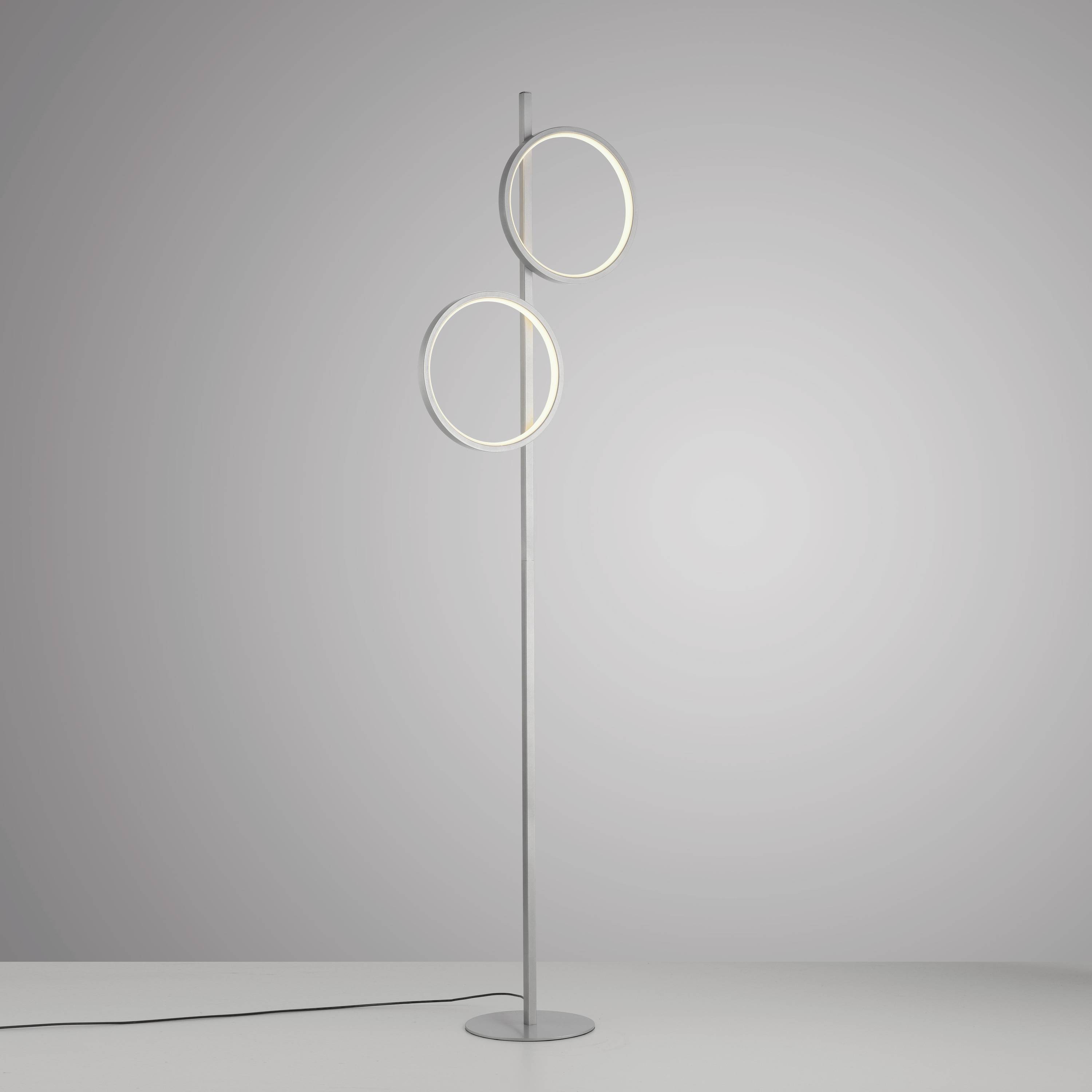 Eine moderne Stehlampe mit zwei leuchtenden, kreisförmigen Ringen auf einem schlanken, vertikalen Ständer, vor grauem Hintergrund.
