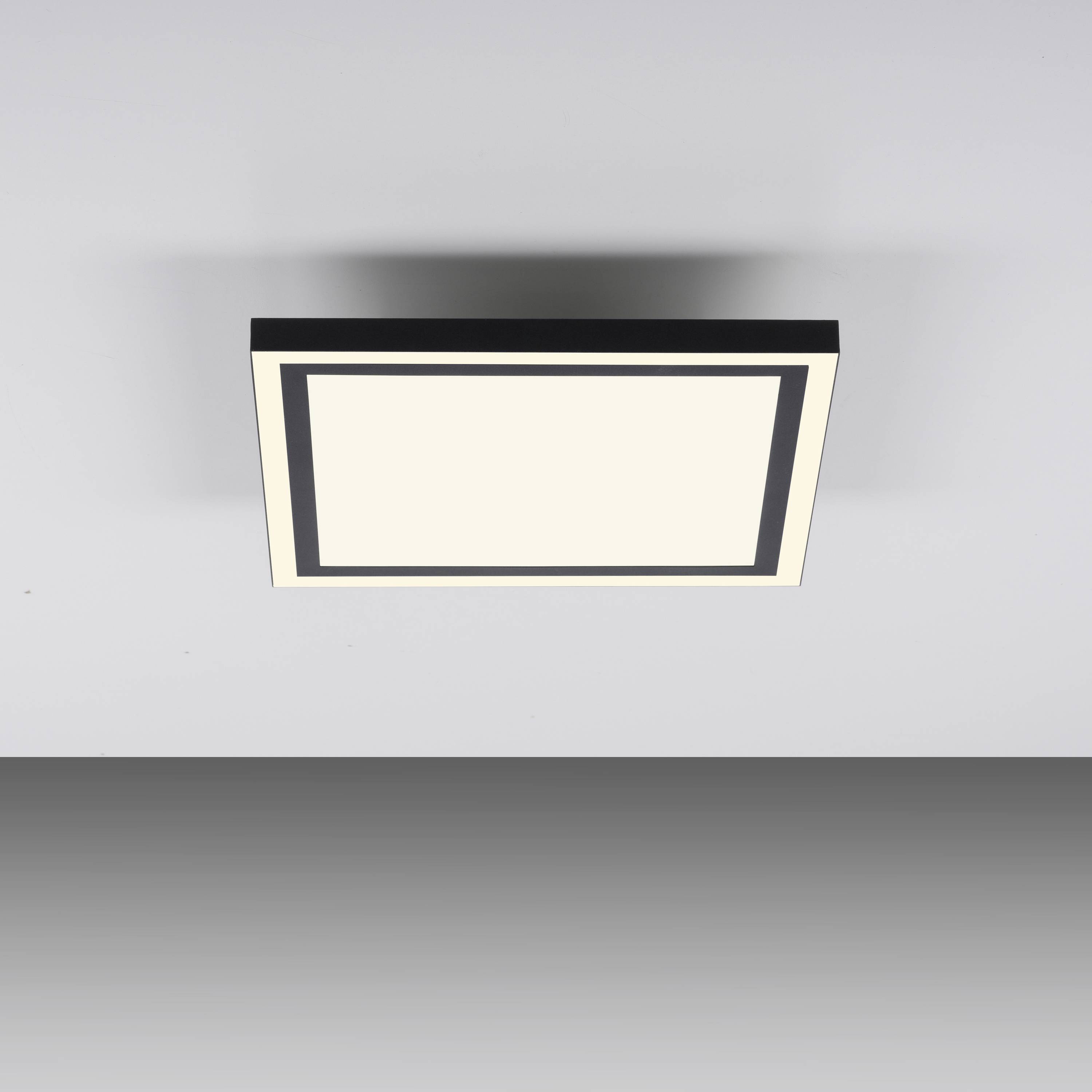 Quadratische Deckenleuchte mit schwarzem Rahmen und weißer Leuchtfläche, an grauer Decke montiert. Minimalistisches Design.