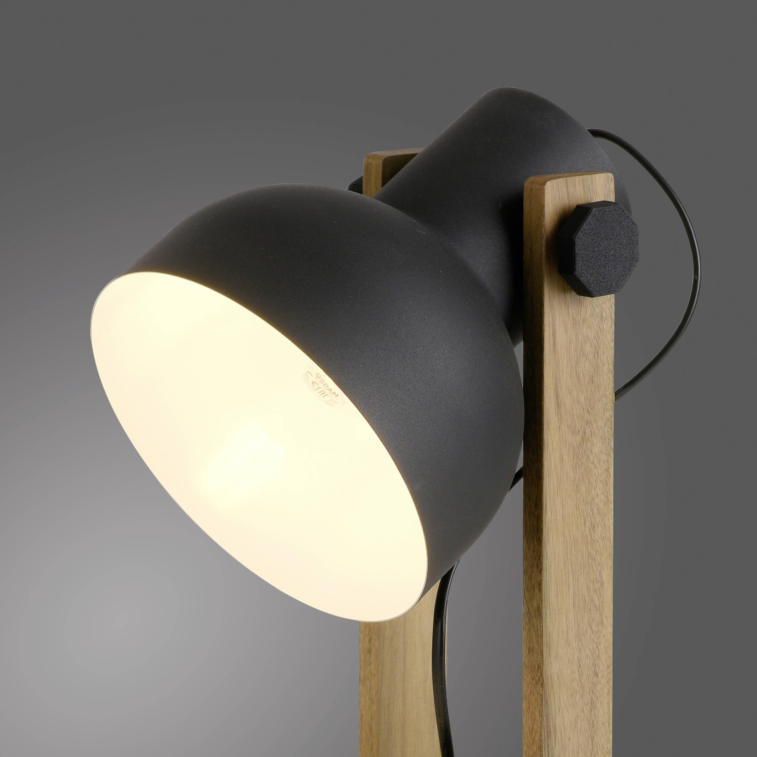 Eine moderne, schwarze Tischlampe mit Holzelementen leuchtet hell gegen einen grauen Hintergrund.