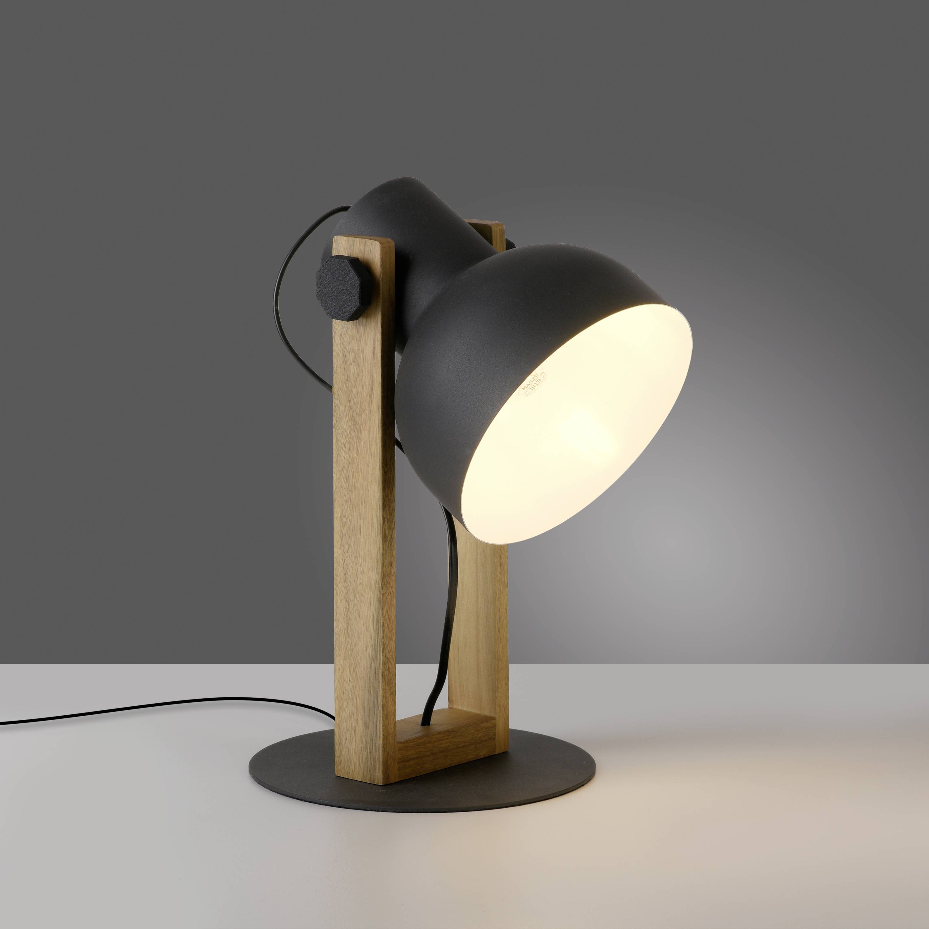 Eine Tischlampe mit schwarzem Metallschirm und Holzgestell spendet warmes Licht auf eine graue Oberfläche.