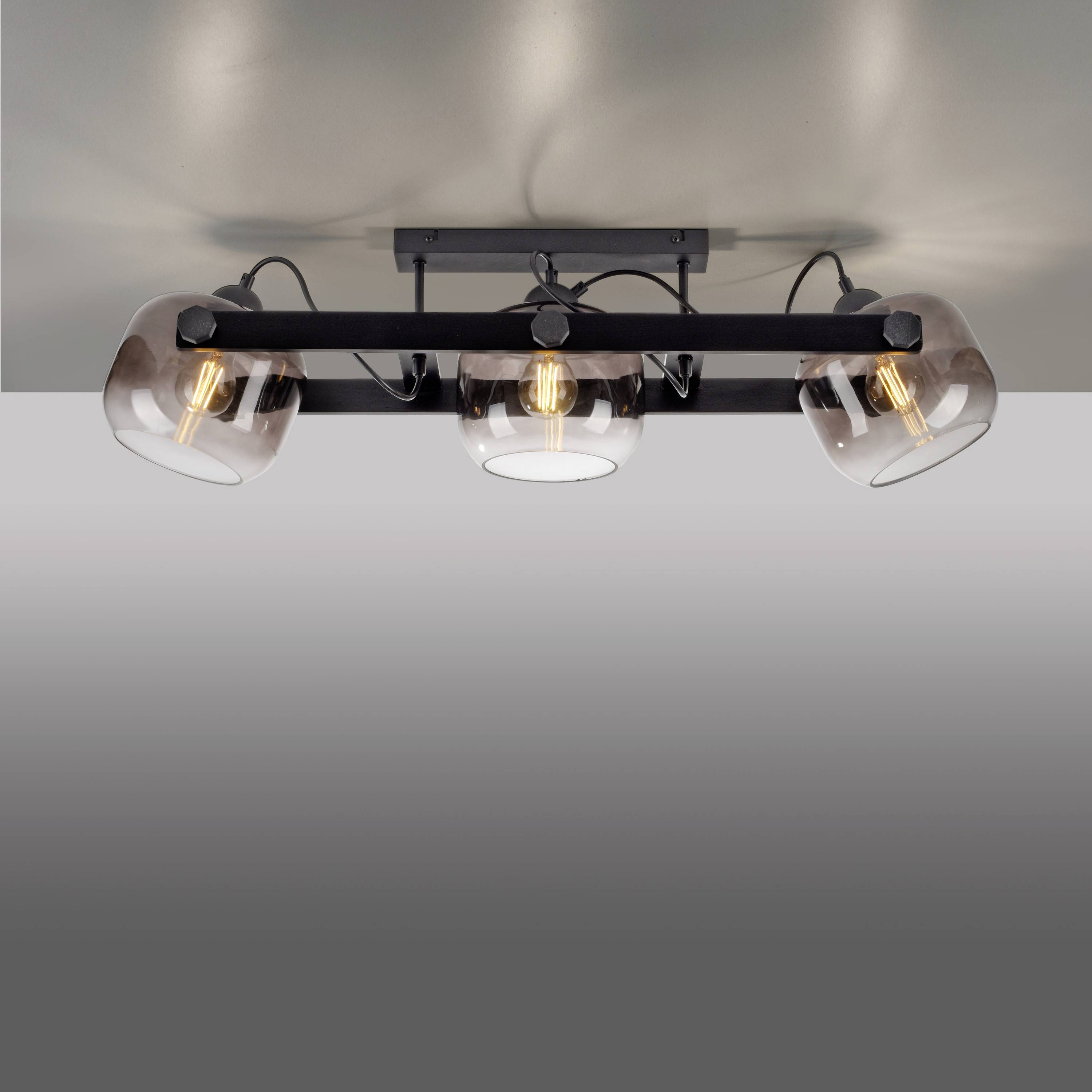 Eine moderne Deckenleuchte mit drei Glühbirnen, montiert auf einer schwarzen Metallhalterung, strahlt warmes Licht aus.