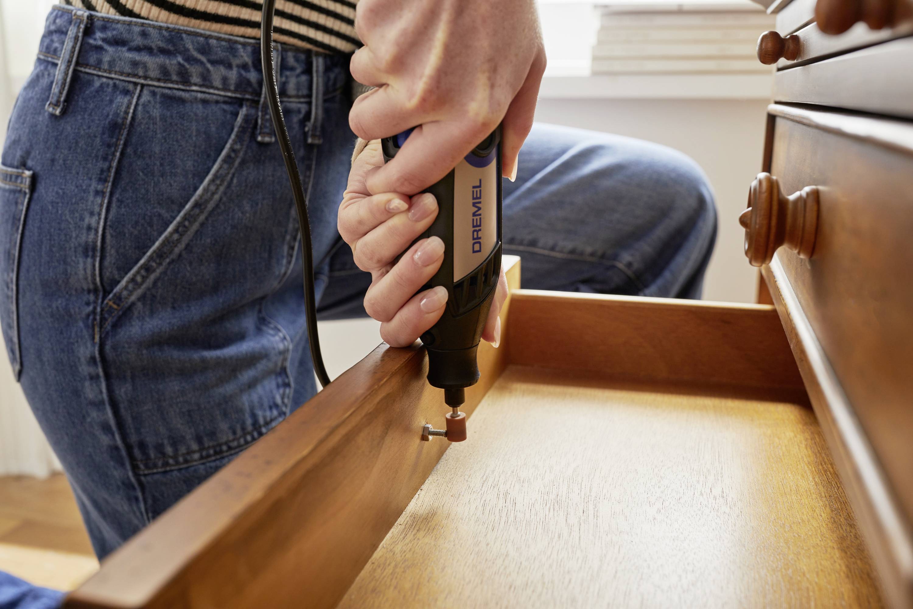 Person bearbeitet eine Holzschublade mit einem Handwerkzeug in einer häuslichen Umgebung.