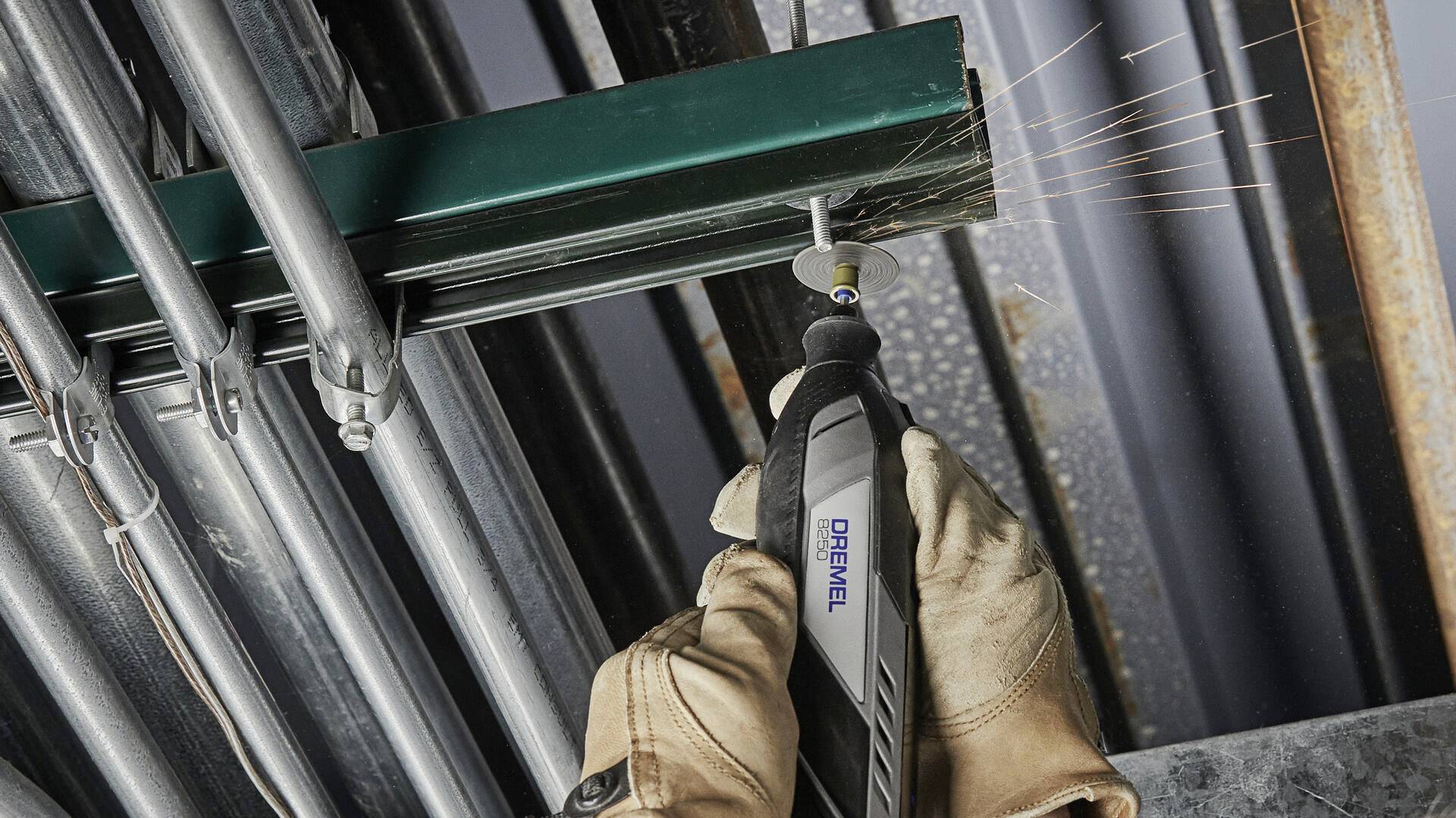 Eine Person schneidet mit einem Dremel-Werkzeug ein Metallrohr. Funken fliegen. Trägt Arbeitshandschuhe für Sicherheit.