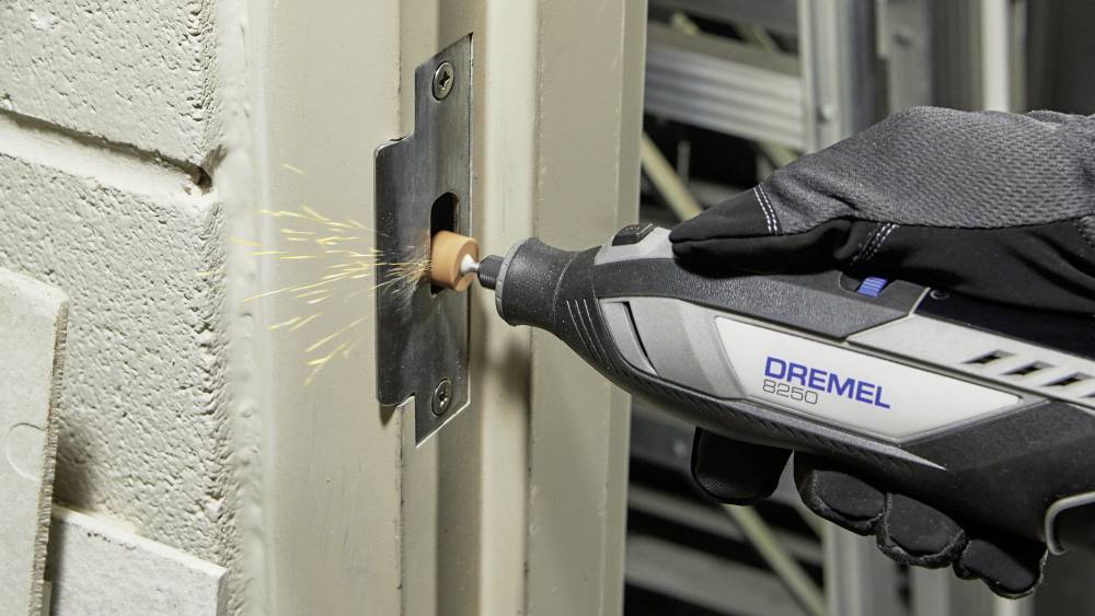 Eine Person schleift mit einem Dremel-Werkzeug einen Metallteil an einer Tür, Funken sprühen. Die Szene zeigt handwerkliches Arbeiten.