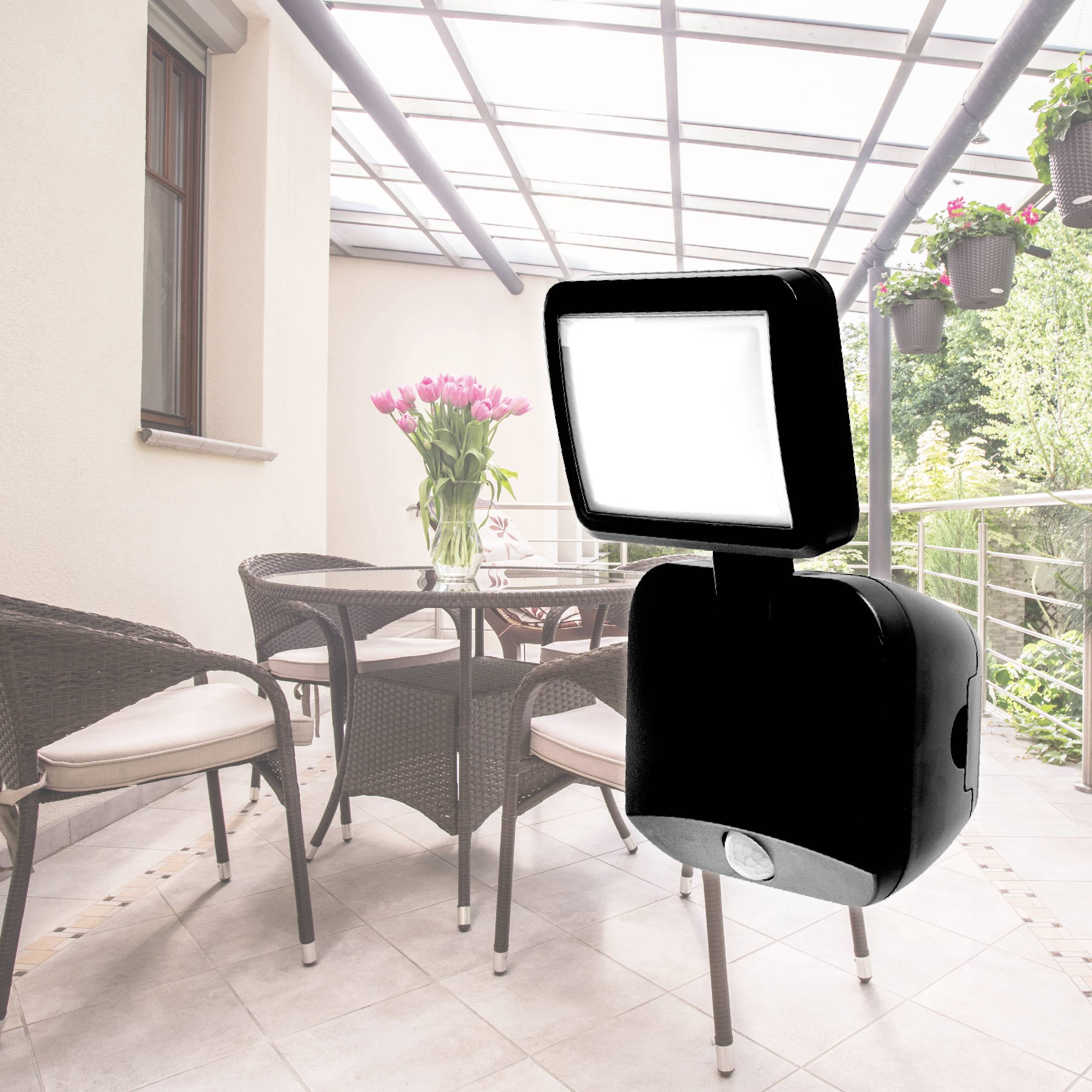 Ein moderner LED-Außenstrahler beleuchtet eine Terrasse mit Korbmöbeln und hängenden Blumen. Ideal für nächtliche Beleuchtung im Freien.