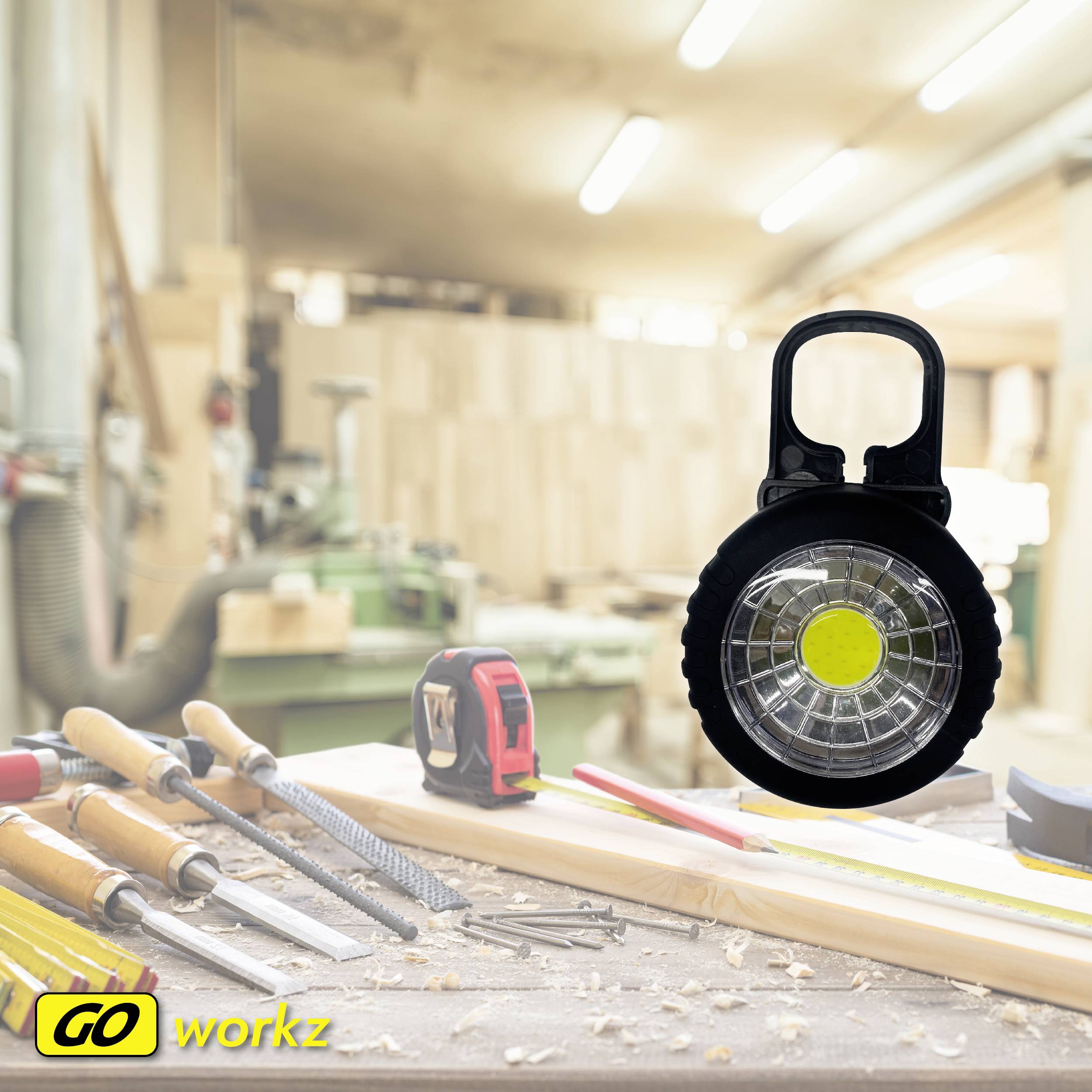 Eine tragbare LED-Arbeitsleuchte steht auf einem Tisch mit verschiedenen Handwerkszeugen in einer gut beleuchteten Werkstatt.