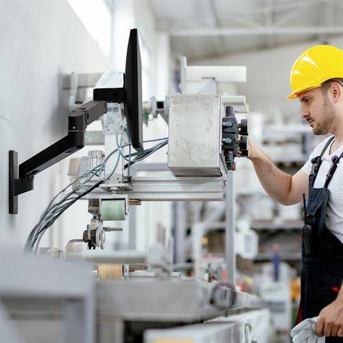 Ein Mann trägt einen gelben Schutzhelm und inspiziert Maschinen in einer industriellen Umgebung.