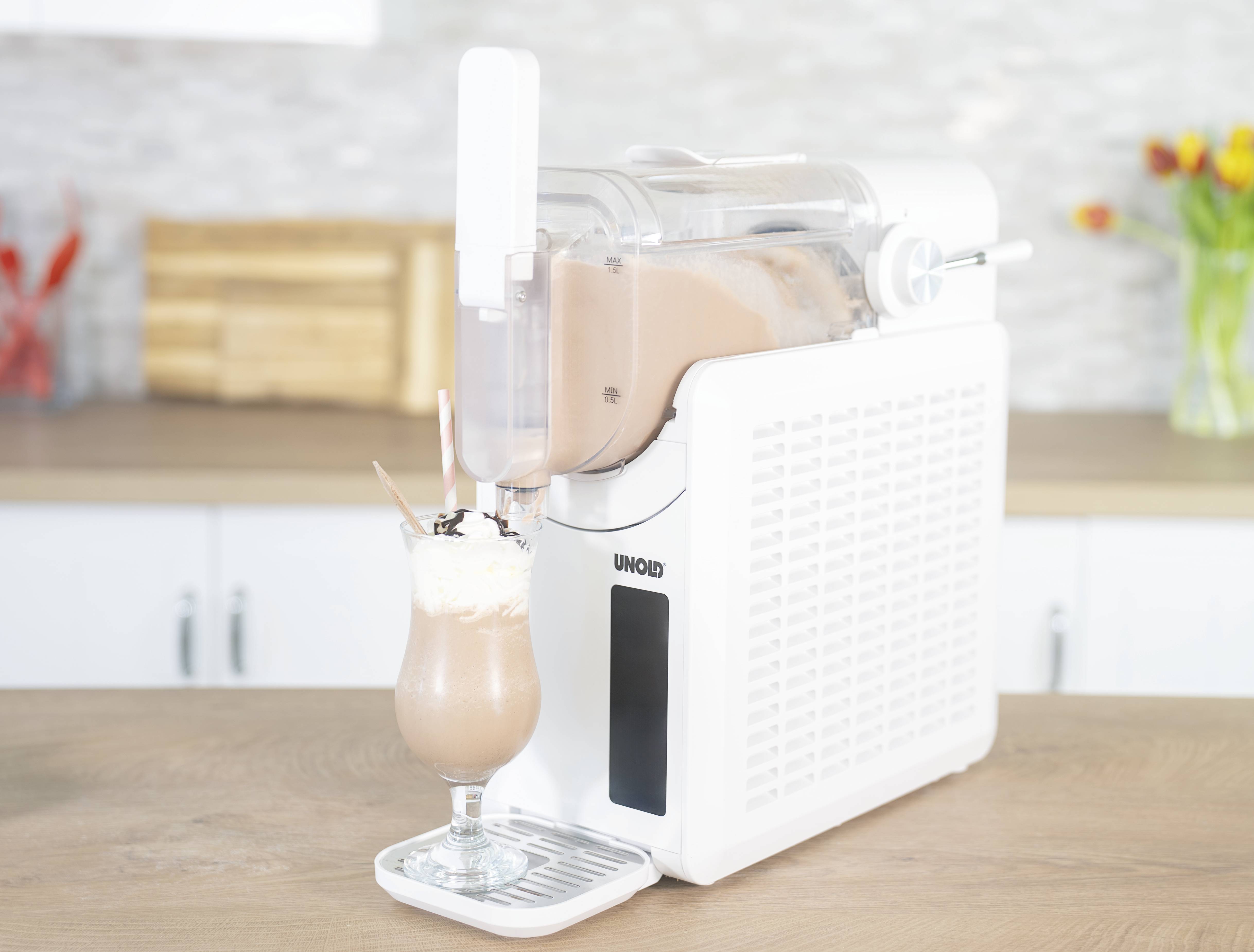 Eine Eismaschine auf einer Küchenarbeitsplatte mit fertigem Eisgetränk im Glas, daneben ein Strauß gelber und roter Tulpen.