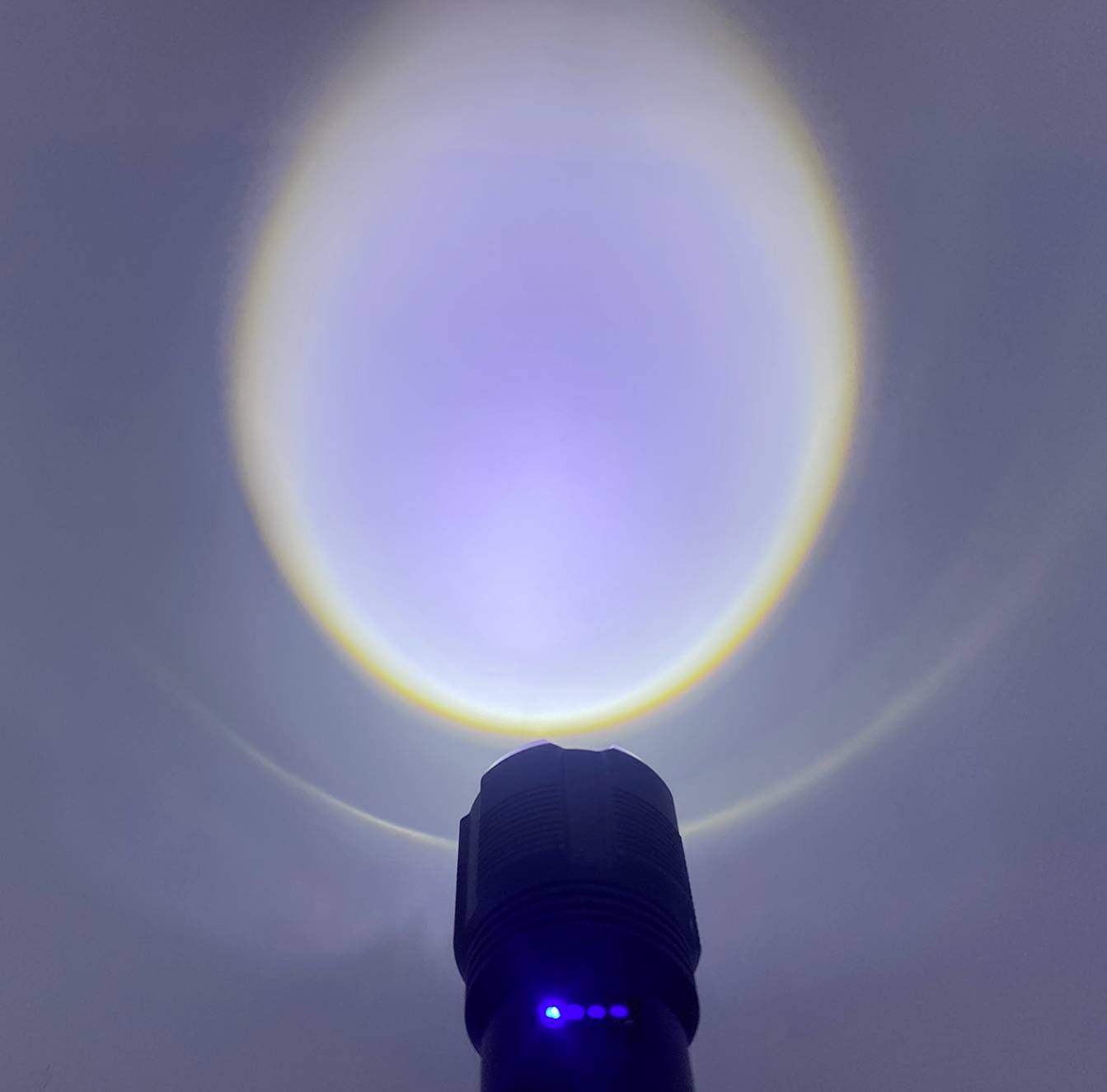 Taschenlampe leuchtet gegen eine Wand und erzeugt einen hellen Lichtkreis mit blauem und gelbem Rand.