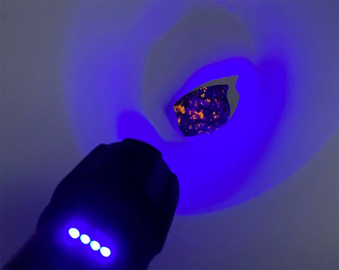 Eine blaue Lichtquelle beleuchtet einen dunklen Stein, wodurch orangefarbene Reflexionen sichtbar werden.