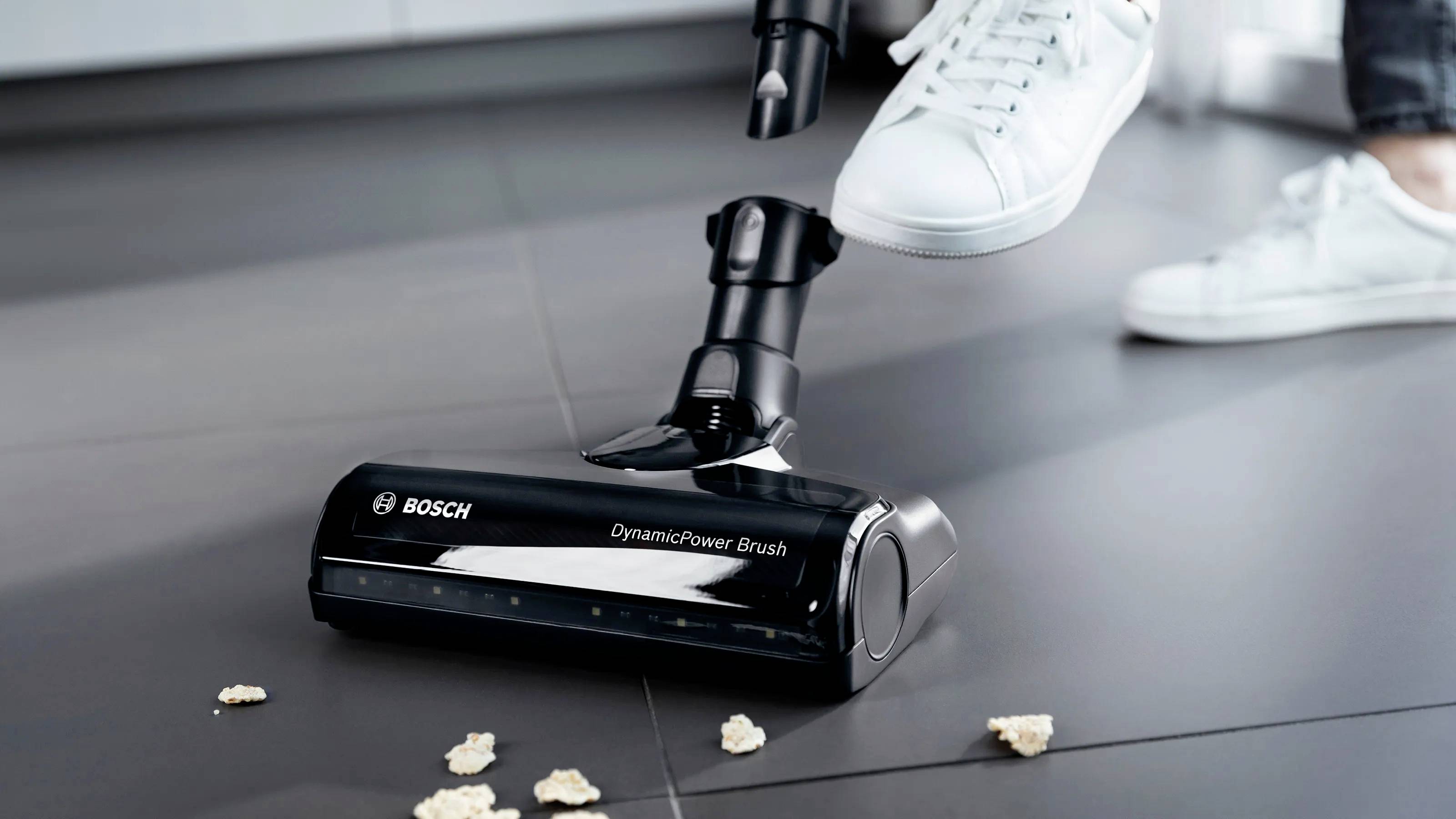Ein Staubsauger saugt Krümel vom Boden auf, während eine Person mit weißen Sneakers daneben steht.