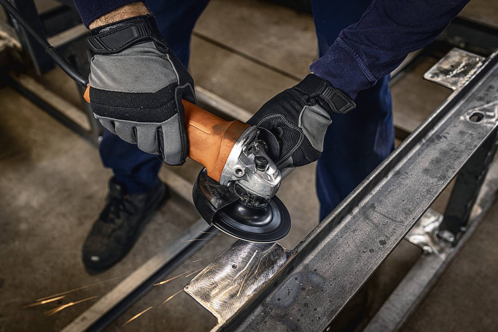 Person schleift Metall mit einer Winkelschleifmaschine; Funken fliegen. Szenerie in Werkstattumgebung.