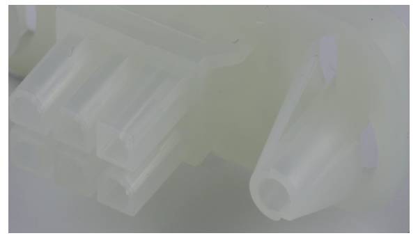 Nahaufnahme eines durchsichtigen Kunststoffverbinders mit mehreren Schlitzen und einer zylindrischen Öffnung, verwendet in der elektronischen oder mechanischen Montage.