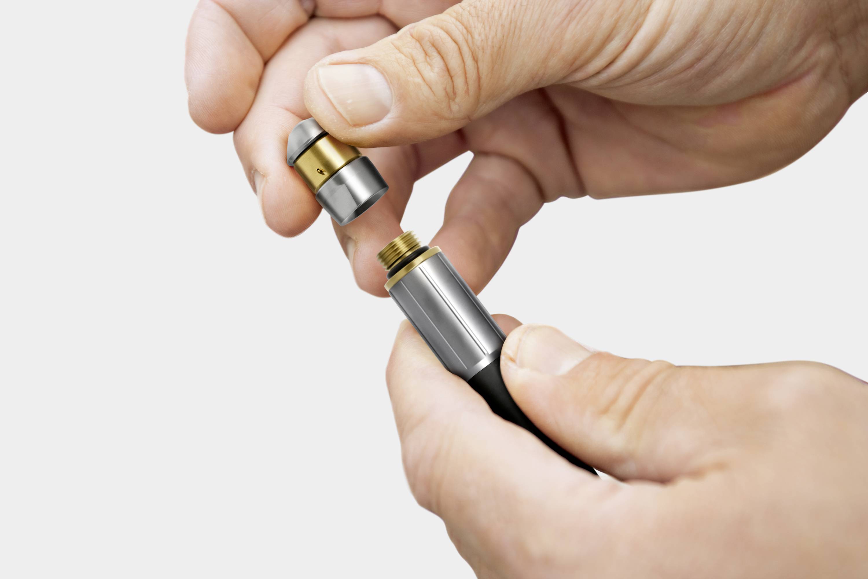 Zwei Hände montieren ein Metallteil auf eine schwarze Vorrichtung. Das Bild zeigt den Zusammenbau eines technischen Geräts.