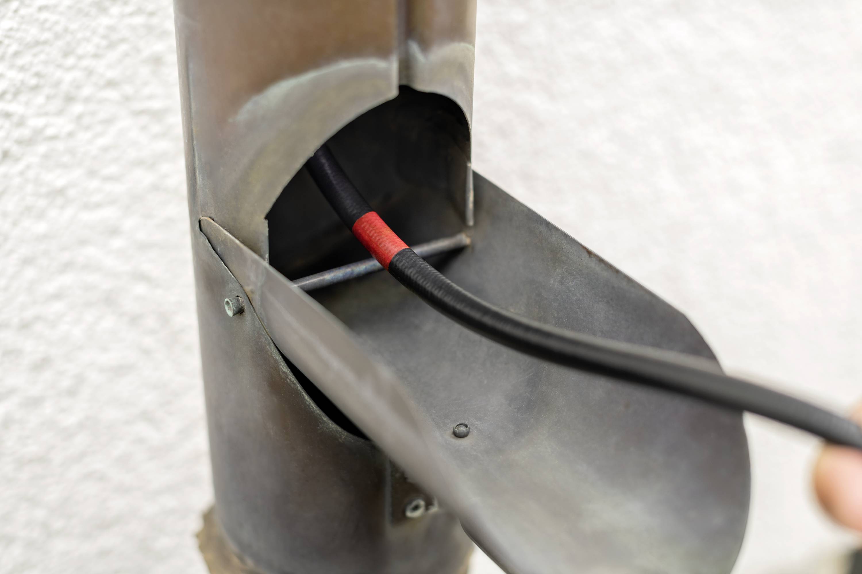 Ein rohrförmiges Metallobjekt, das ein schwarzes, rot markiertes Kabel enthält, das durch eine Öffnung verläuft.
