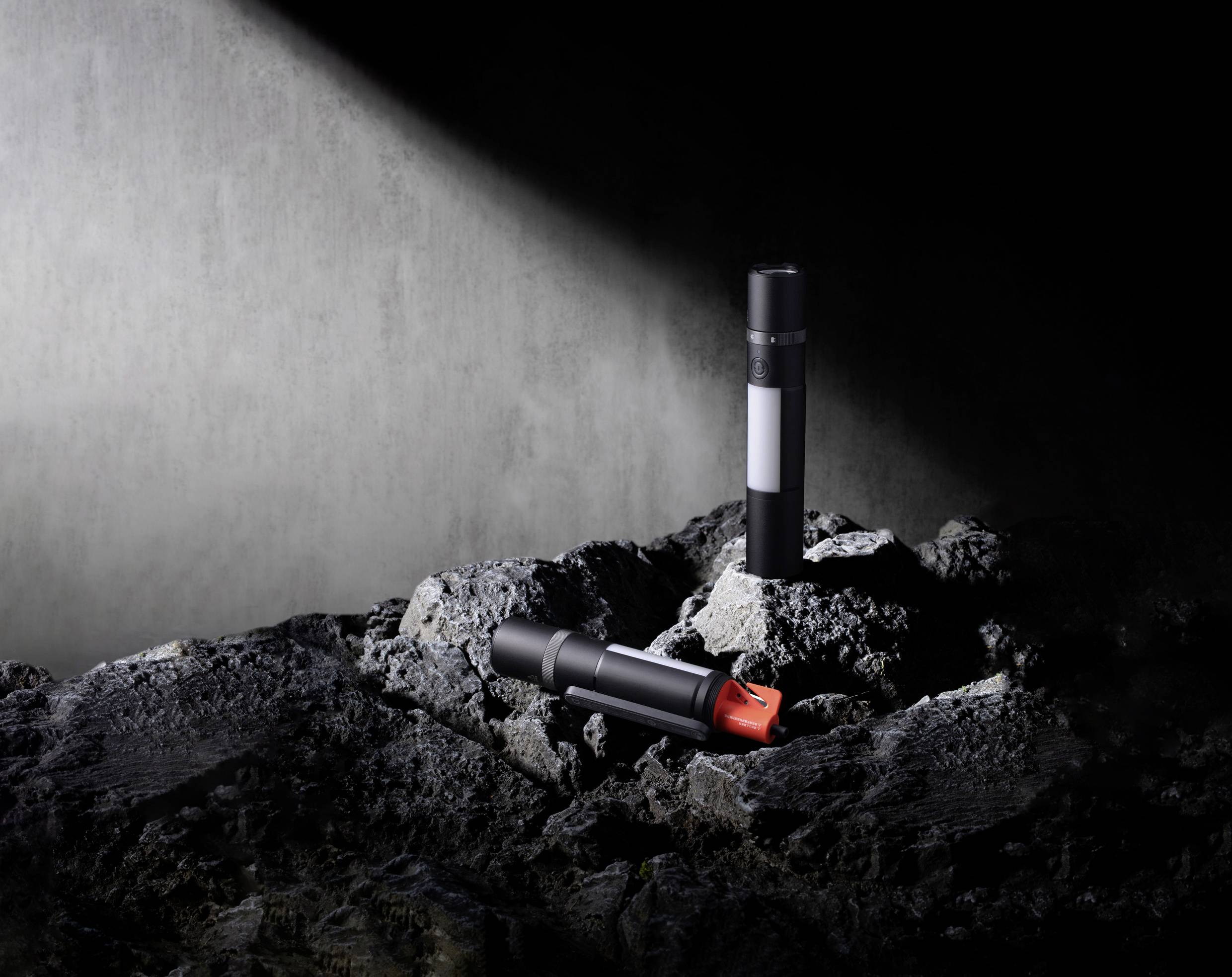 Zwei schwarze Zylinder auf einer felsigen Oberfläche im Spotlight, einer hat eine rote Kappe. Atmosphäre: geheimnisvoll und futuristisch.