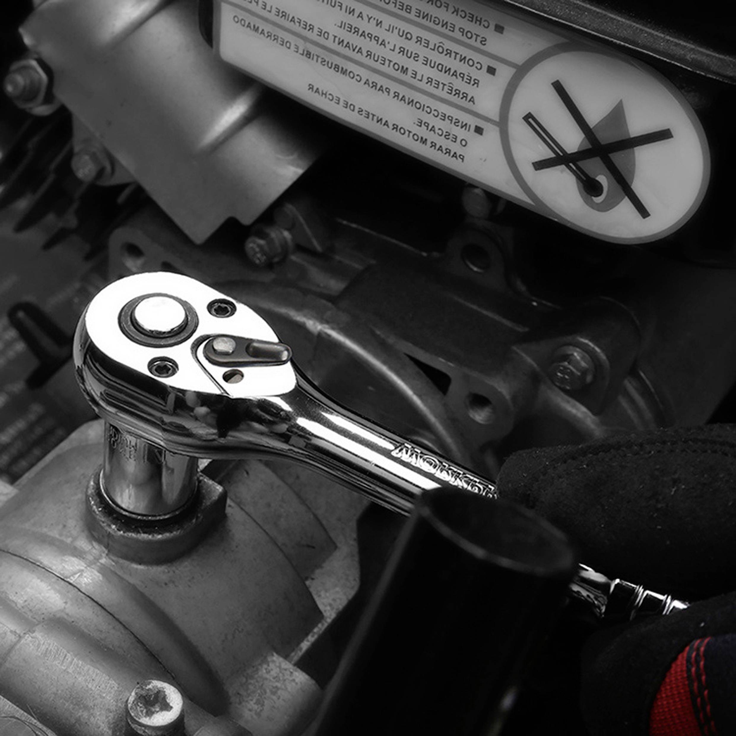 Eine Person verwendet einen Ratschenschlüssel, um ein Teil an einem Motor einzustellen, wobei über ihr ein Sicherheitswarnsymbol mit einer Hand und einem durchgestrichenen Schraubschlüssel angebracht ist.