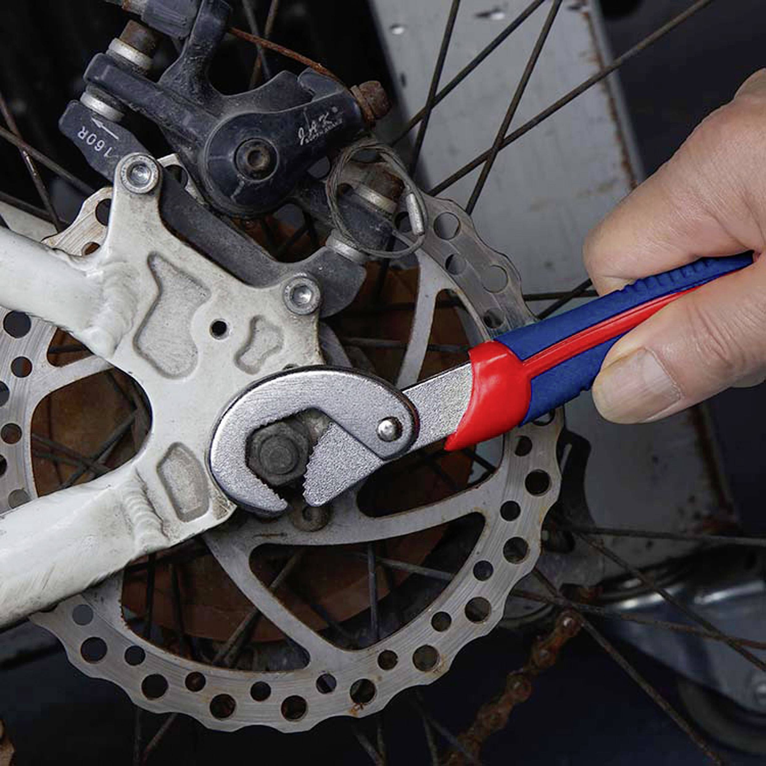 Eine Hand, die einen Schraubenschlüssel benutzt, um eine Fahrrad-Scheibenbremse einzustellen und dabei eine Wartungs- oder Reparaturaktivität am Bremsmechanismus durchführt.